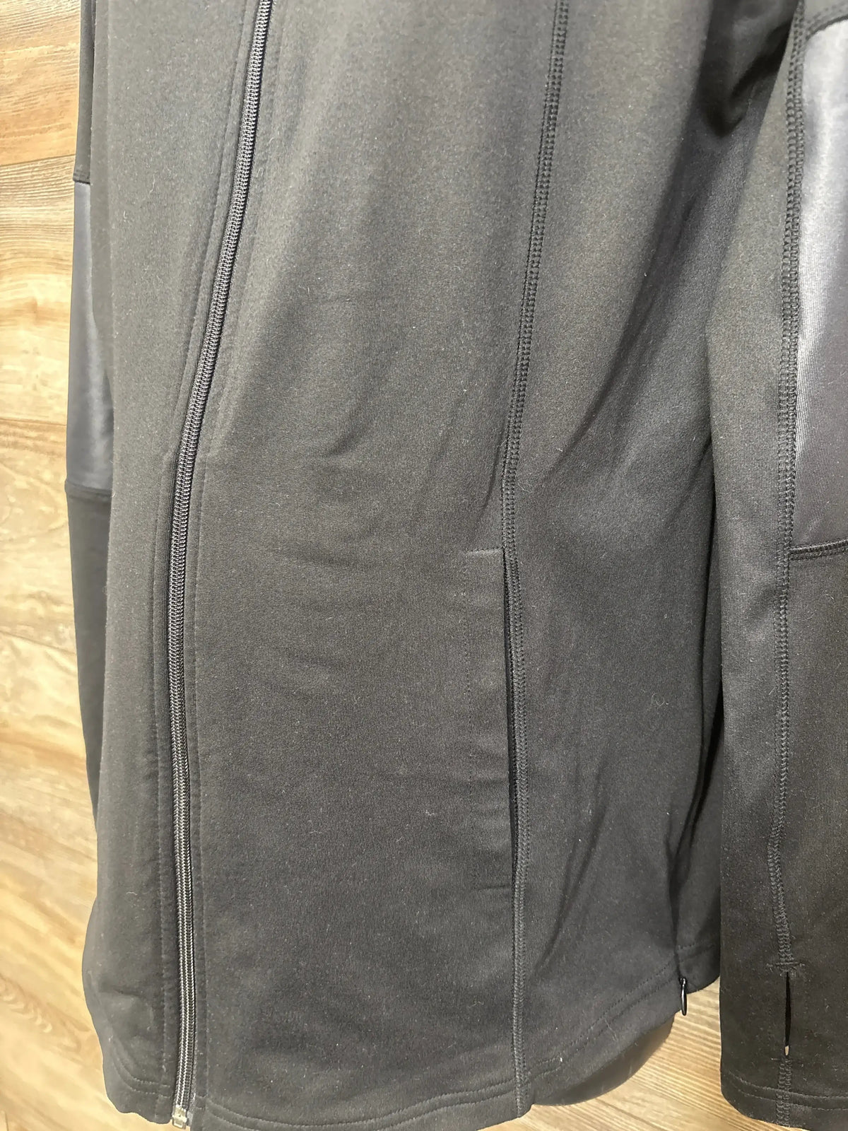 Close-up front view of Isabel maternity active side zip jacket in black, size XL, showcasing side zip panels on wood floor