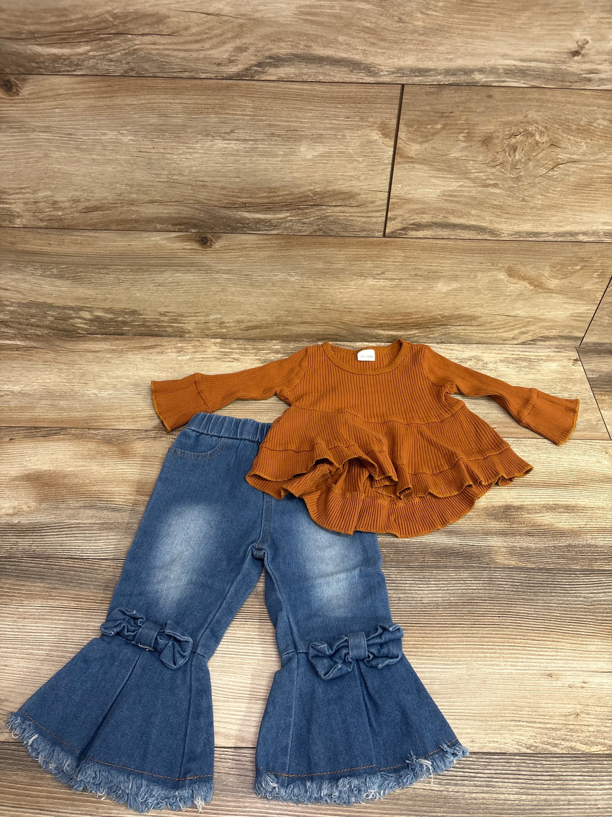 Overhead view of Kucnuzki 2pc ribbed long sleeve top and bell bottom jeans with bows and frayed hems on wood floor