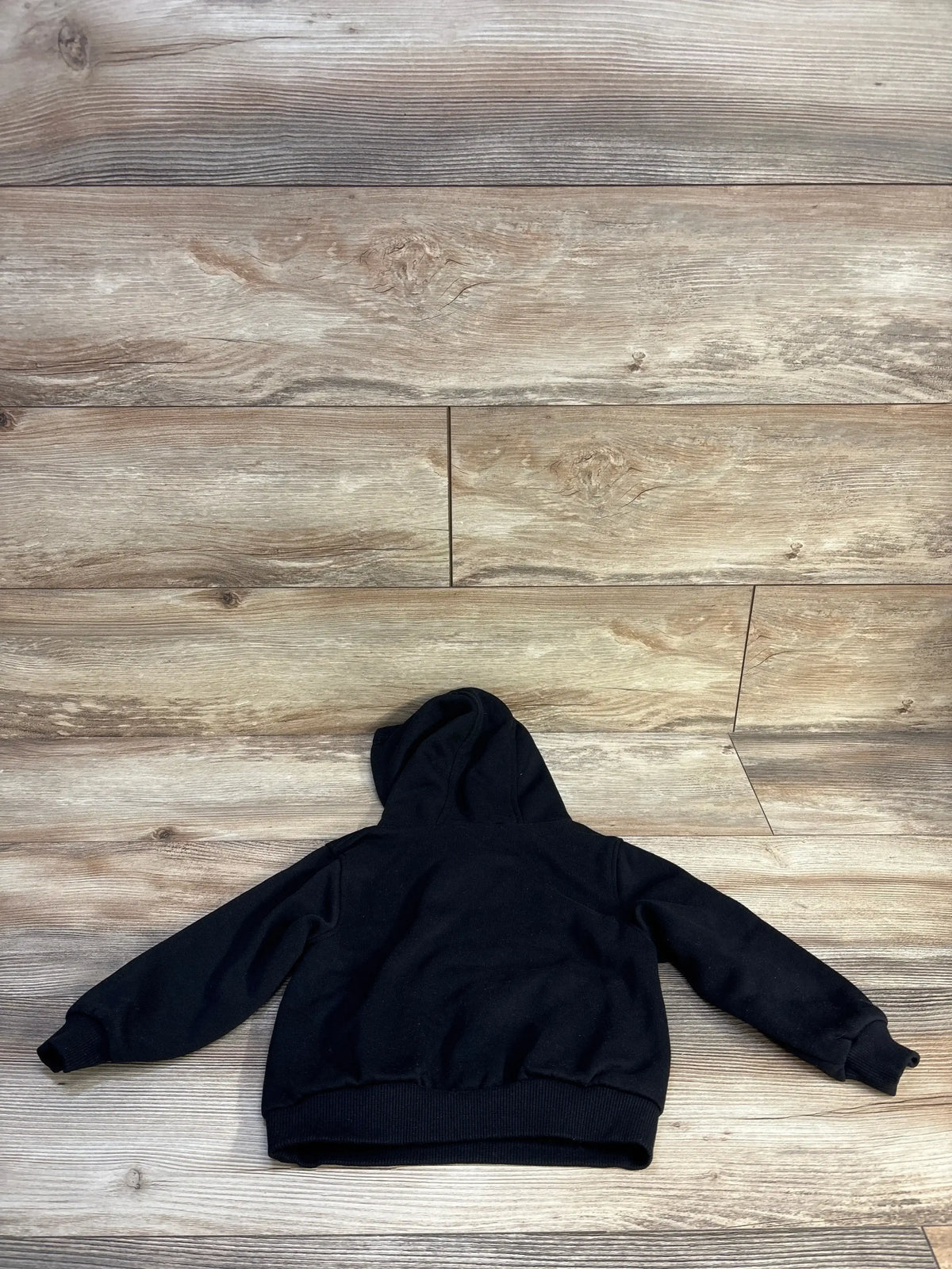 Back view of toddler black Nike pullover hoodie (24 months) showing hood, long sleeves, and ribbed cuffs on light wood floor