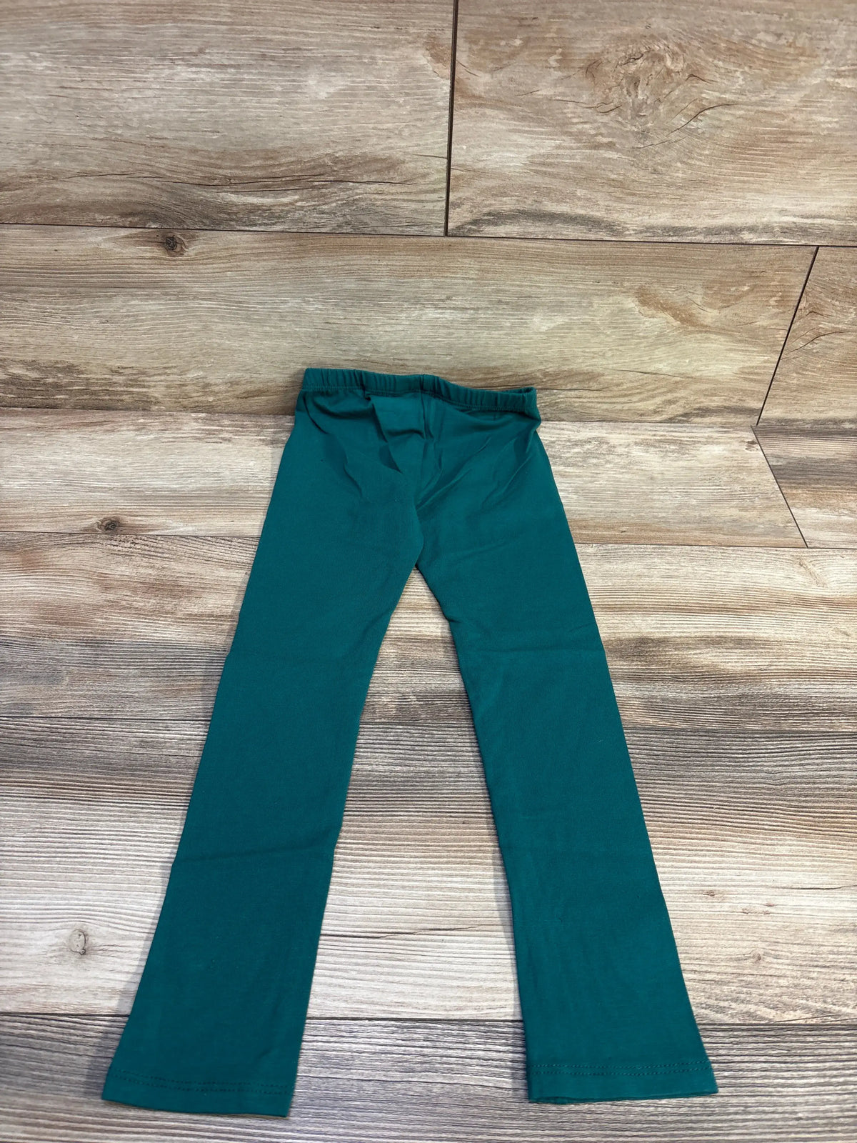 Flat lay of Cat & Jack toddler leggings in green, size 5T, showing elastic waistband and full-length legs on wood background