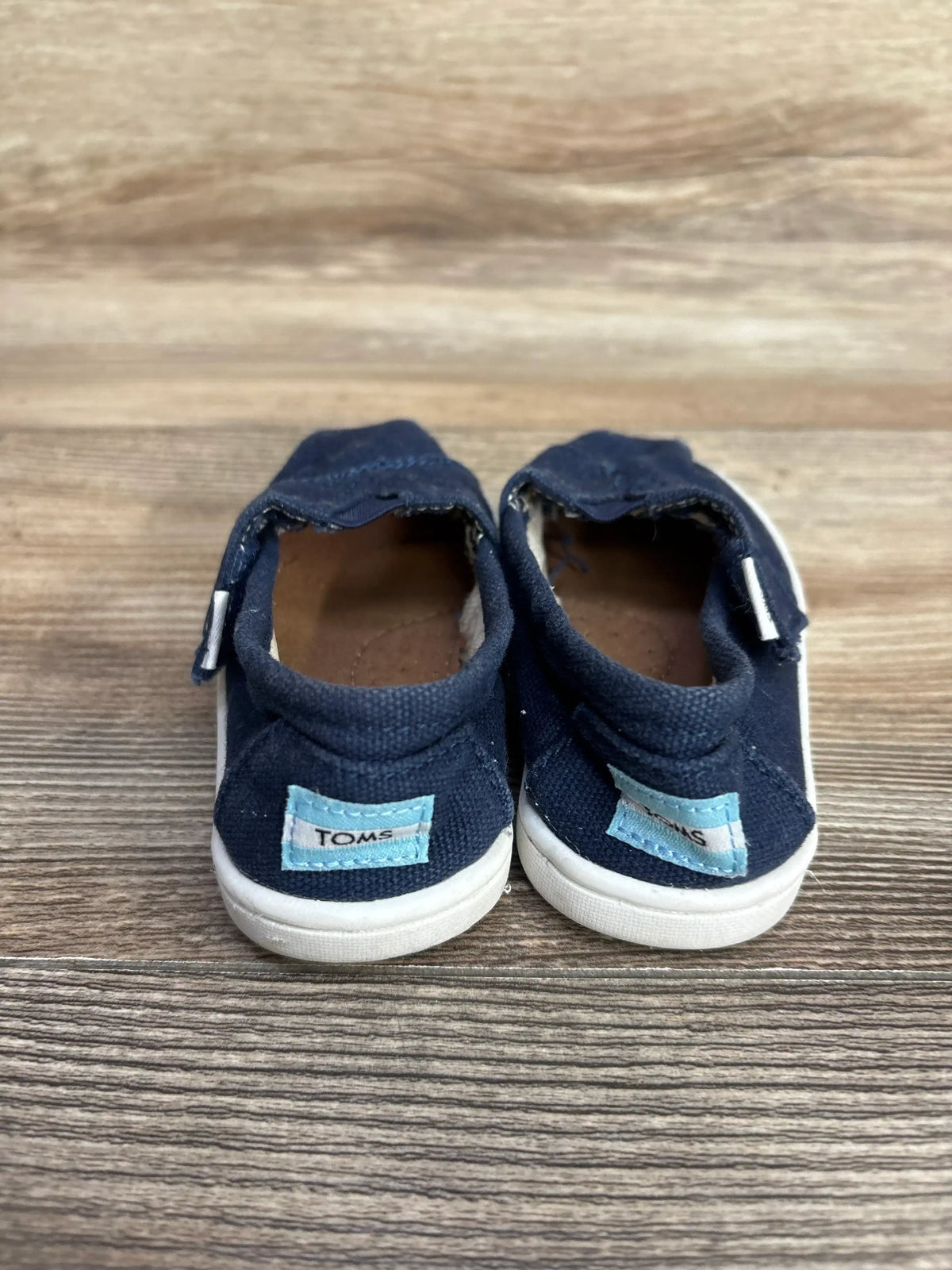 Navy blue toddler TOMS shoes with white soles on wood background.