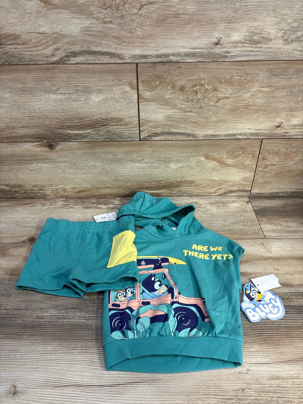 Front view of Bluey teal sleeveless hoodie and bottoms set showcasing vehicle graphic and Are We There Yet text on wood floor