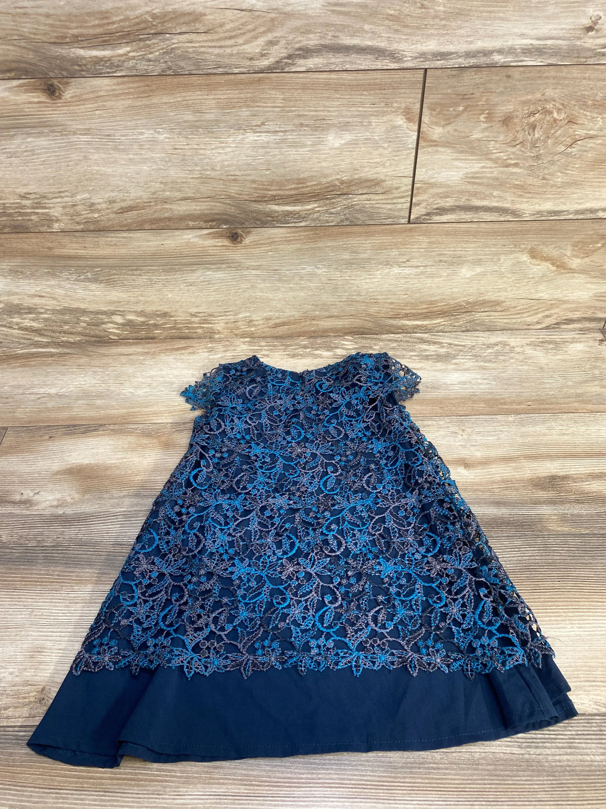 Flat lay of Zara navy blue toddler dress with floral lace overlay, cap sleeves and scalloped hem on light wood floor