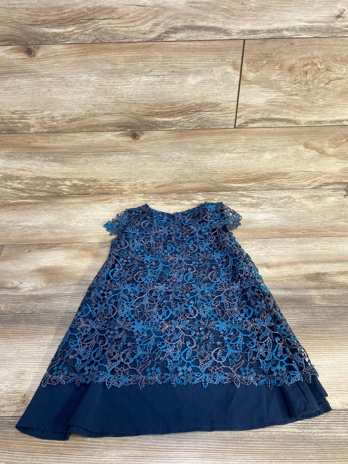 Flat lay of Zara navy blue toddler dress with floral lace overlay, cap sleeves and scalloped hem on light wood floor