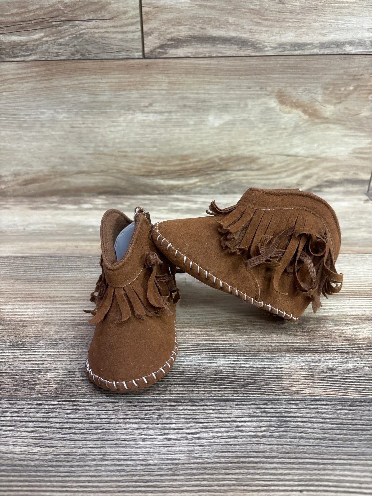 Front and side views of brown cowboy soft sole boots showcasing fringe tassels and white stitching on a wood-grain background