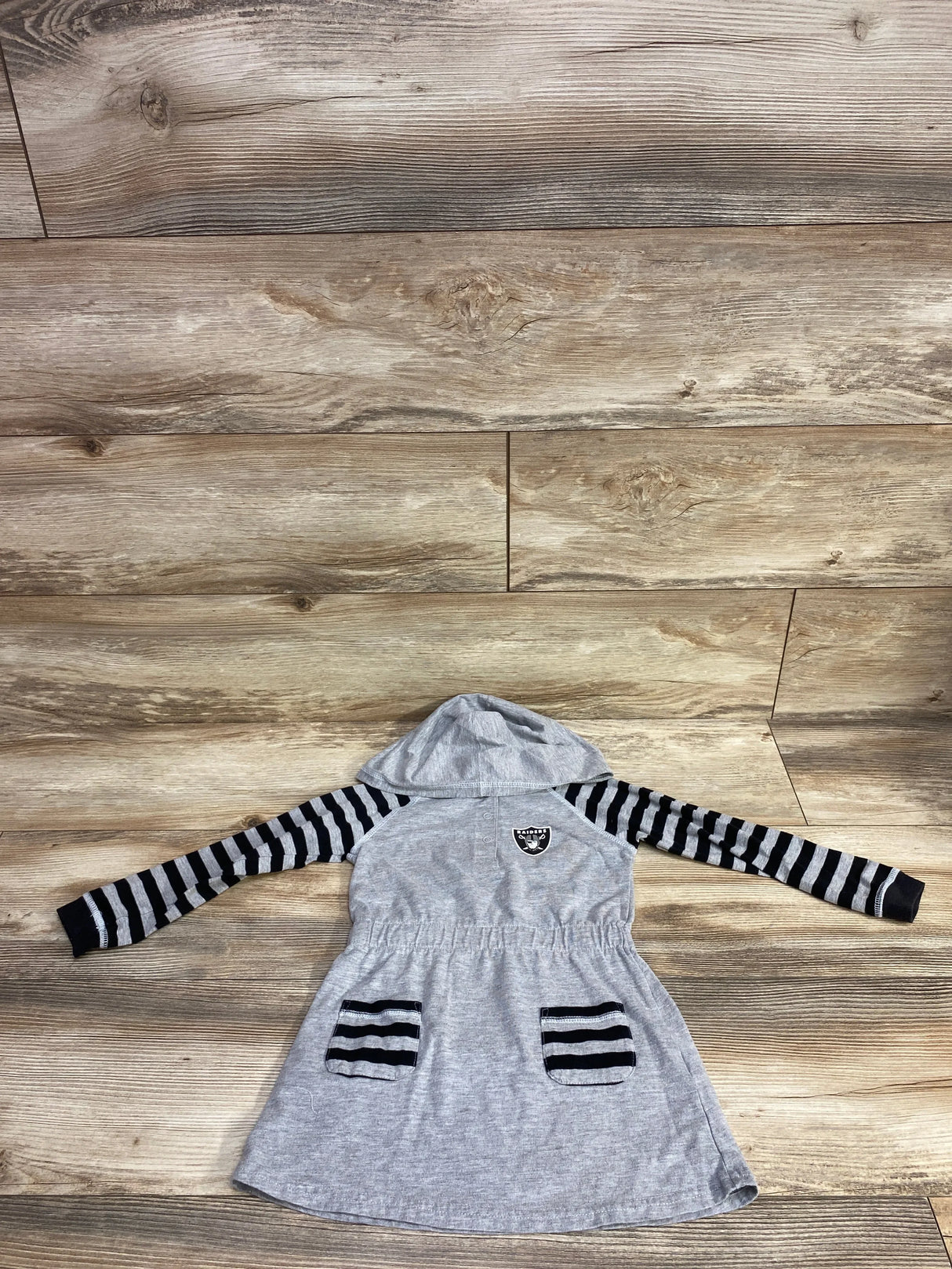 Gray hooded girls dress with black striped long sleeves and pockets, laid flat on wood floor