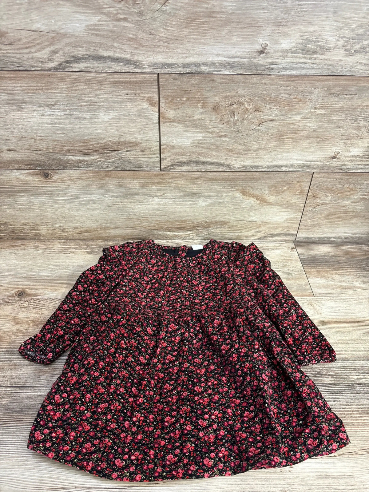 Long sleeve toddler floral dress with small red flowers on black background, laid flat on wood floor