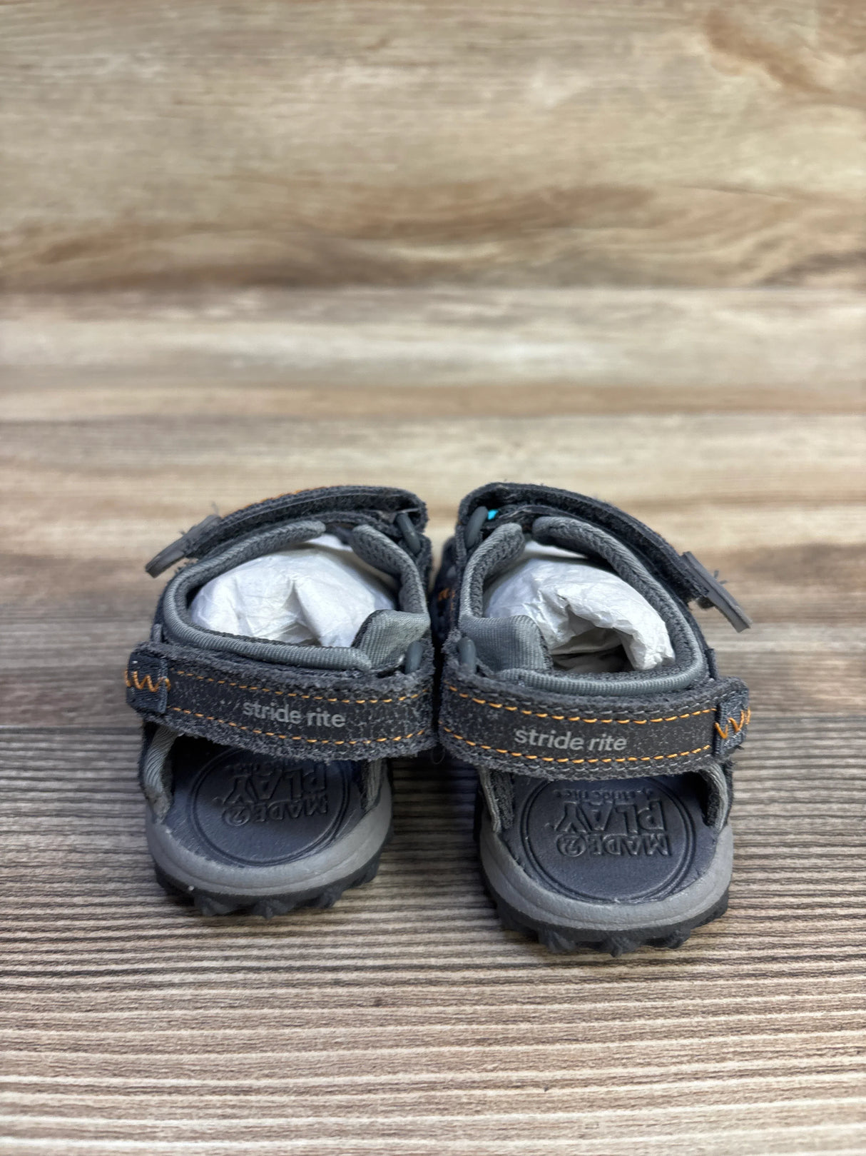 Rear view of gray Stride Rite sandals showing Velcro straps with orange stitching and molded footbed on wood background