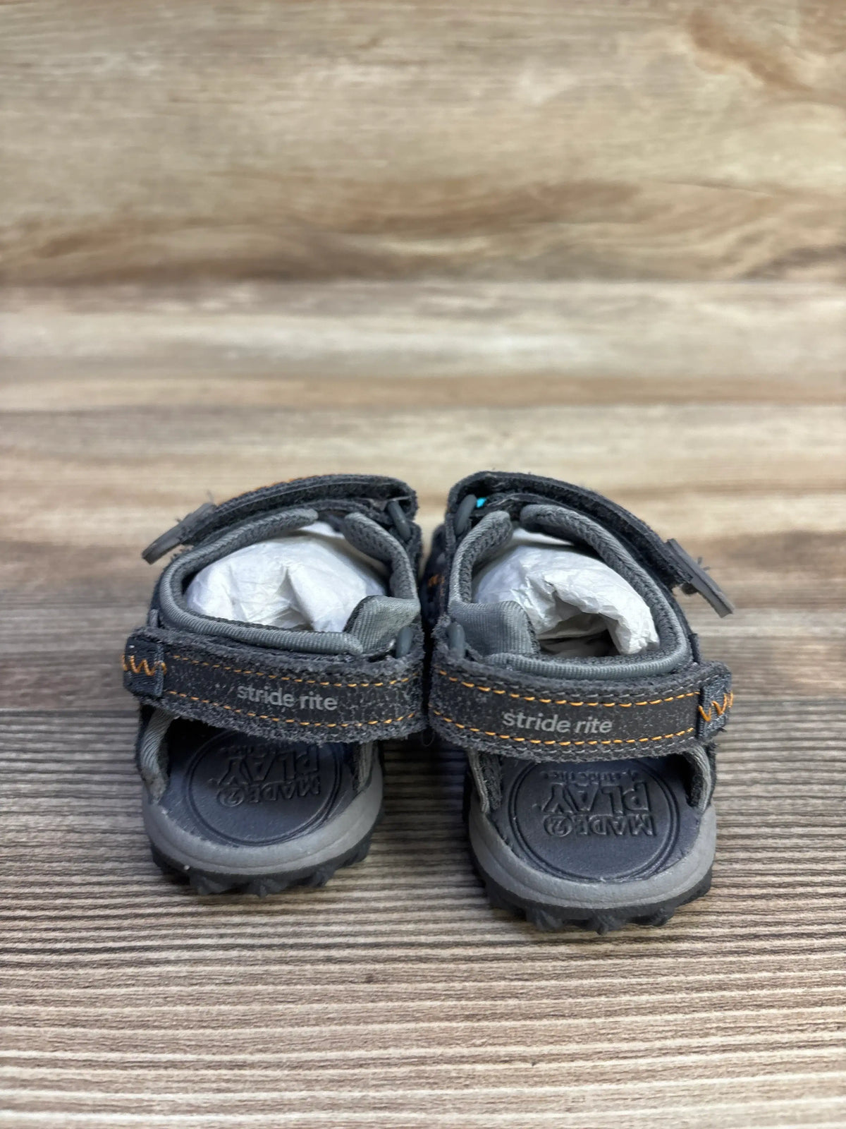 Rear view of gray Stride Rite sandals showing Velcro straps with orange stitching and molded footbed on wood background