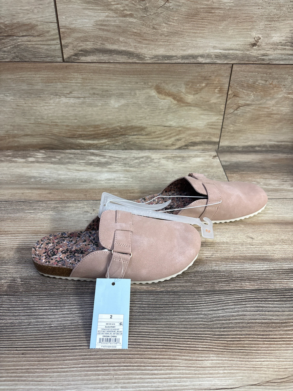 Angled overhead of Cat and Jack clogs in blush showing buckle strap, floral insole, white ridged sole on wood floor