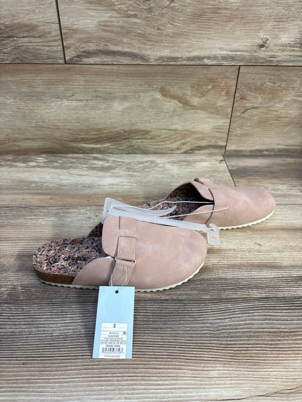 Angled overhead of Cat and Jack clogs in blush showing buckle strap, floral insole, white ridged sole on wood floor