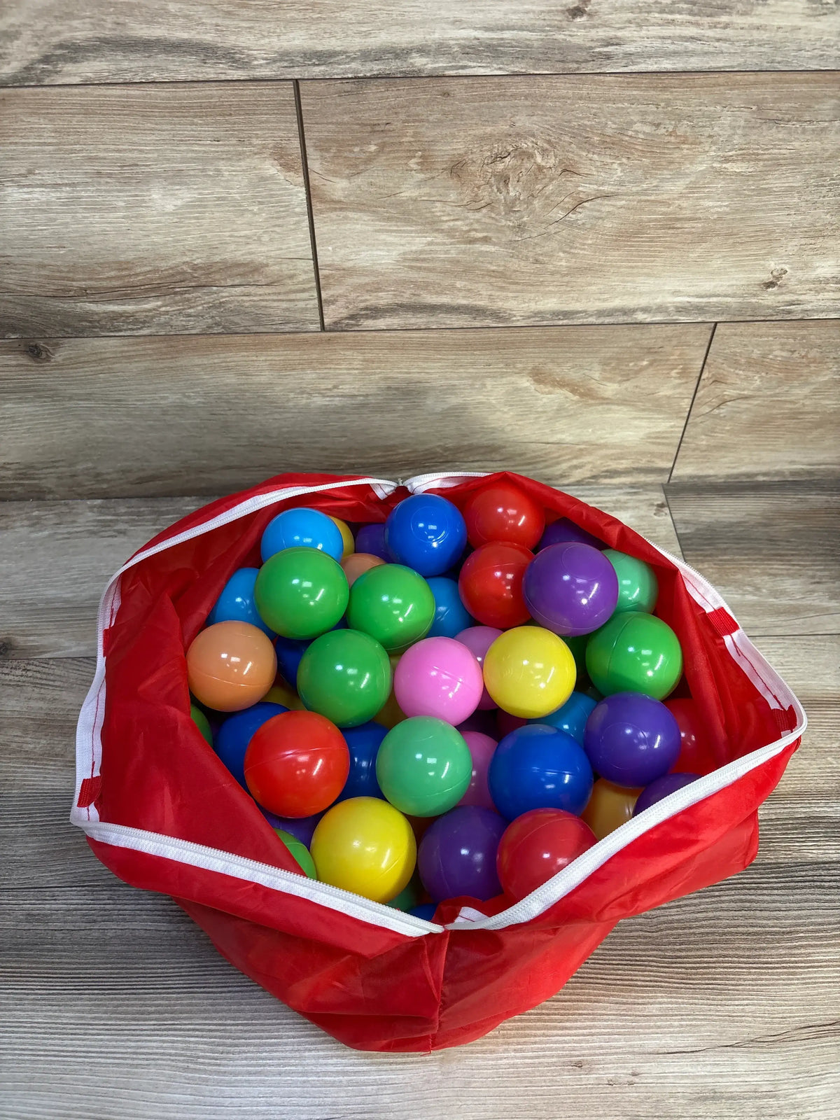 Top view of Bestway multicolor plastic ball pit balls showcasing colorful smooth balls in a red storage bag on a wood floor