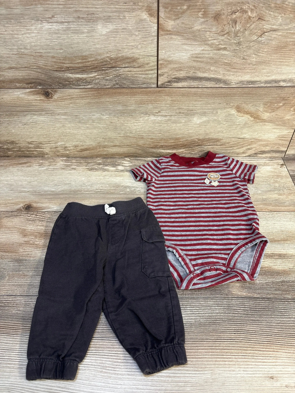 Baby outfit with red striped bodysuit and black pants on wood background