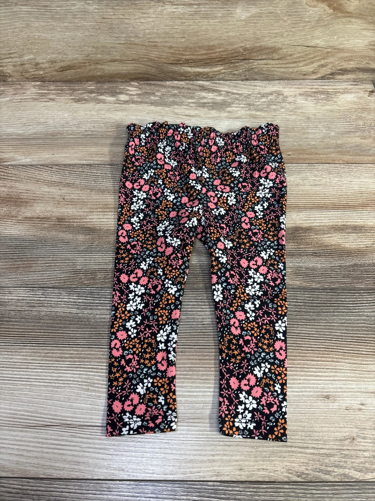 Flat lay of Cat and Jack black leggings with pink and white ditsy floral print and ruffle waistband on wood plank background