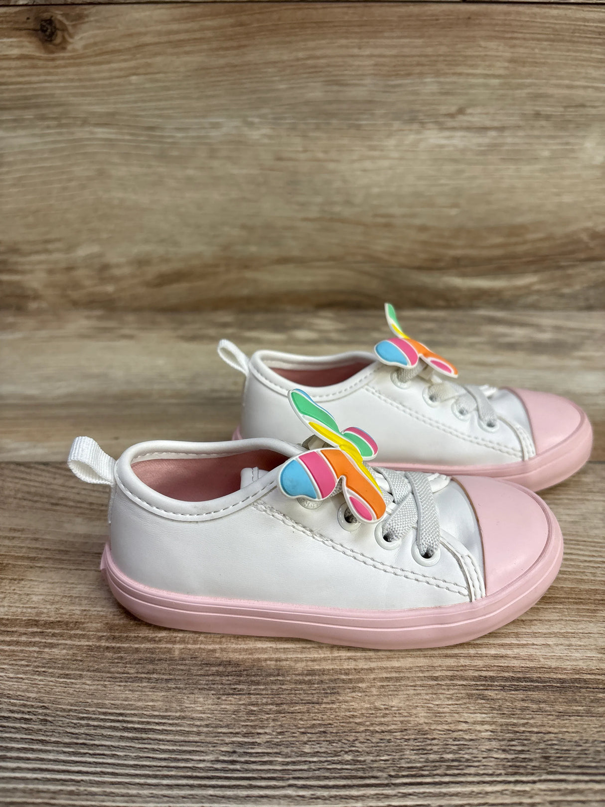 White toddler sneakers with pink rubber soles and colorful butterfly decorations on wooden surface