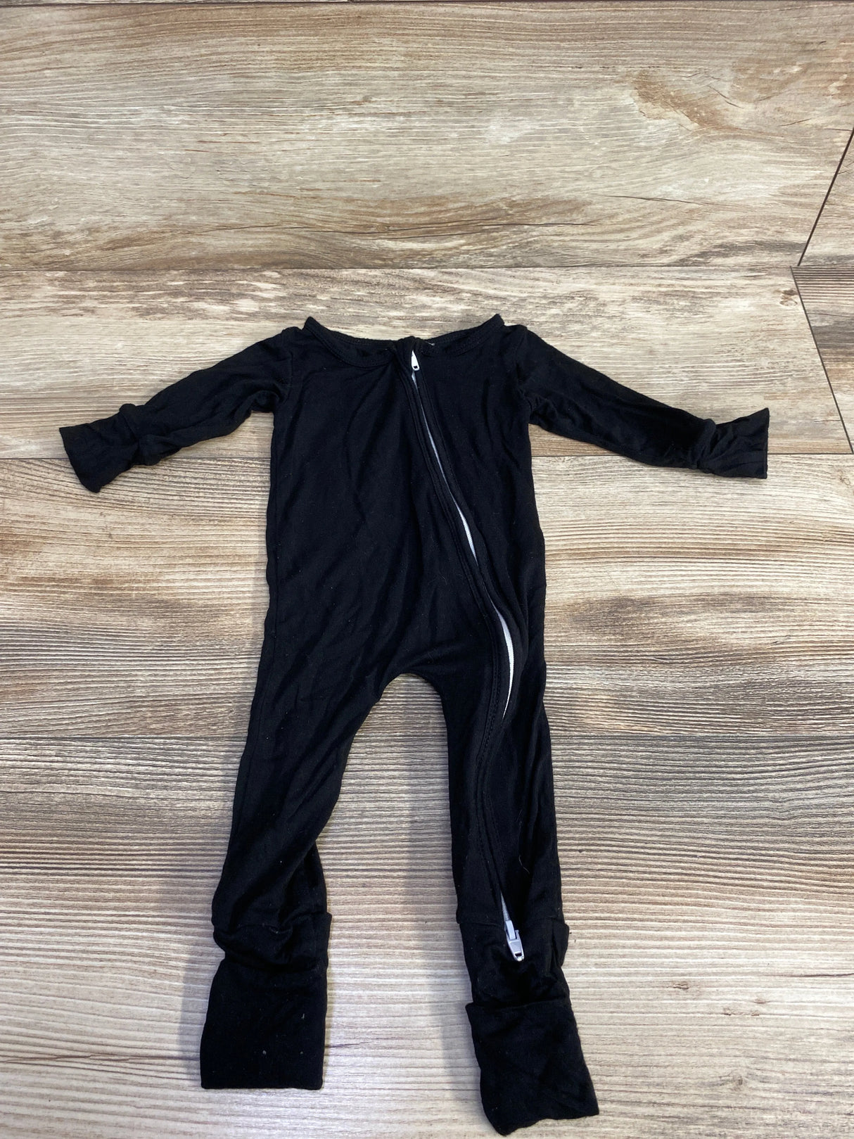Black long-sleeve toddler onesie with diagonal zipper on wooden floor, kids clothes resale