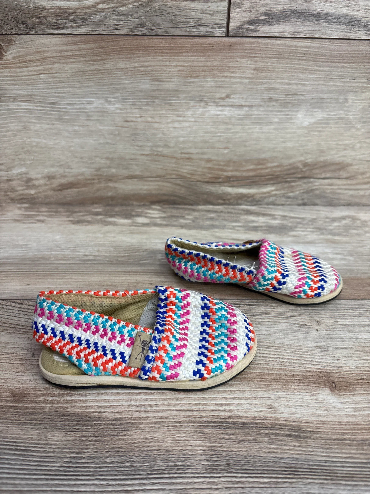 Pair of colorful woven toddler shoes with multicolor stripes on wooden surface