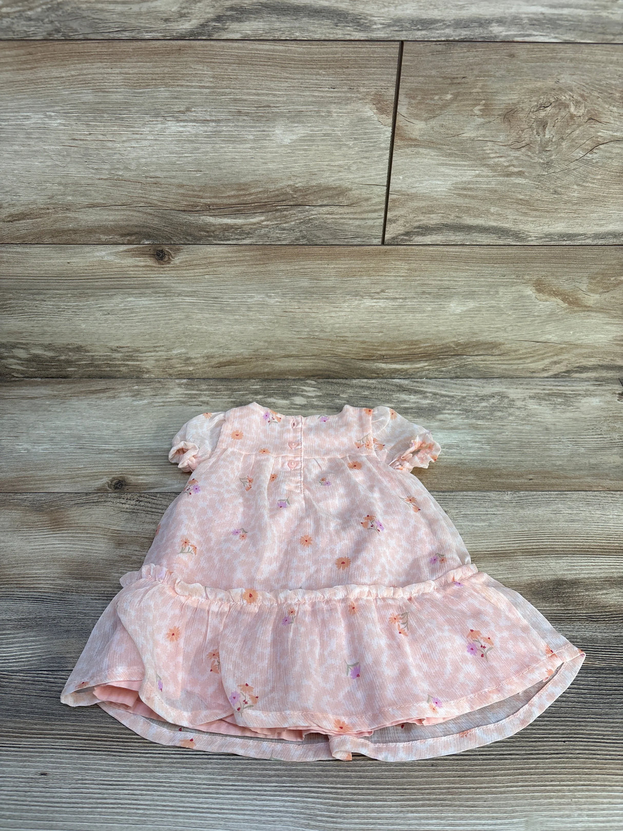 Flat lay of pink Just One You baby dress and matching bloomers showcasing floral print, puff sleeves and ruffled tiered hem on wood floor background