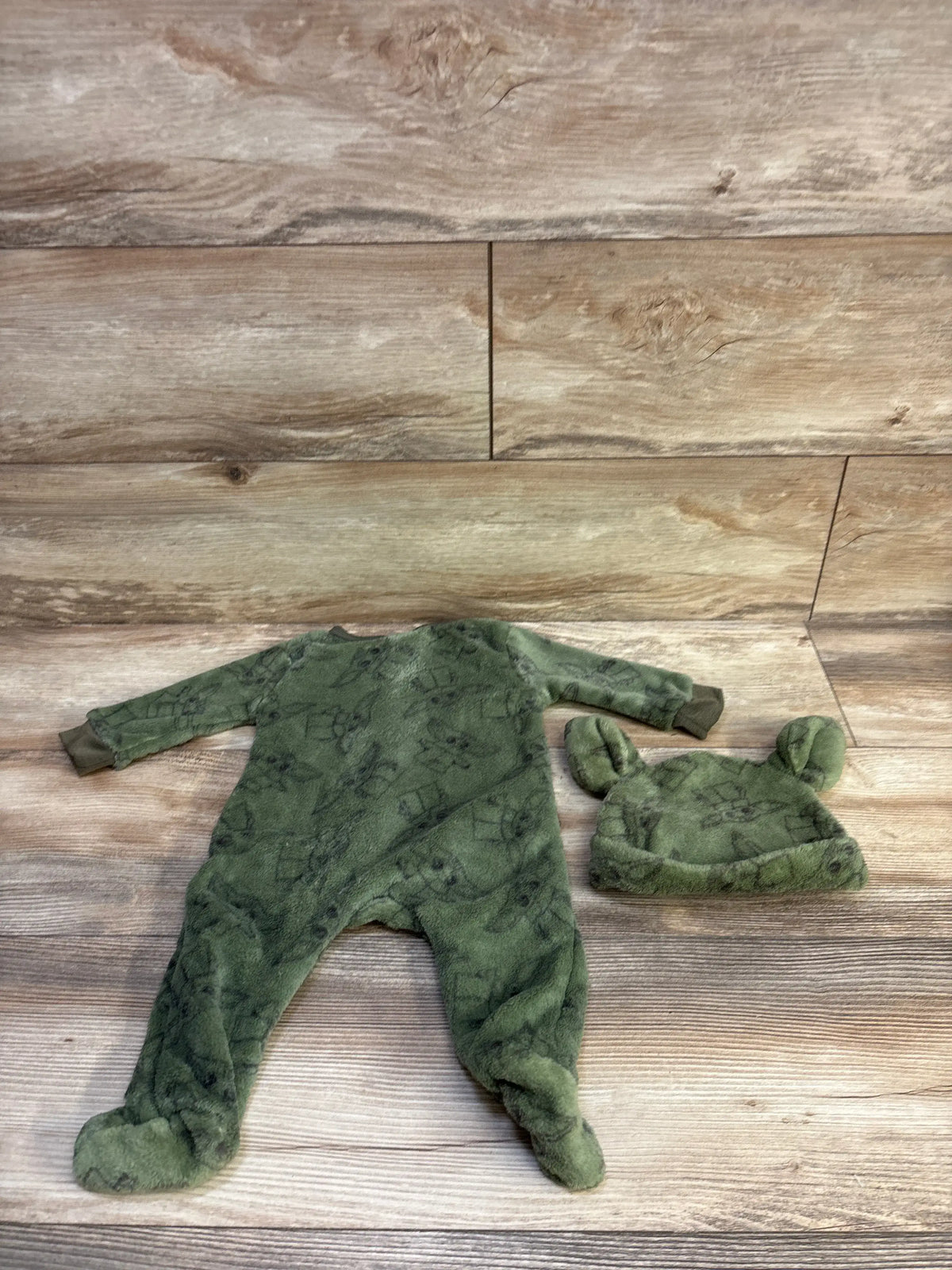 Overhead view of green Star Wars blanket sleeper and matching hat with character print and ear-like details on wood-look floor