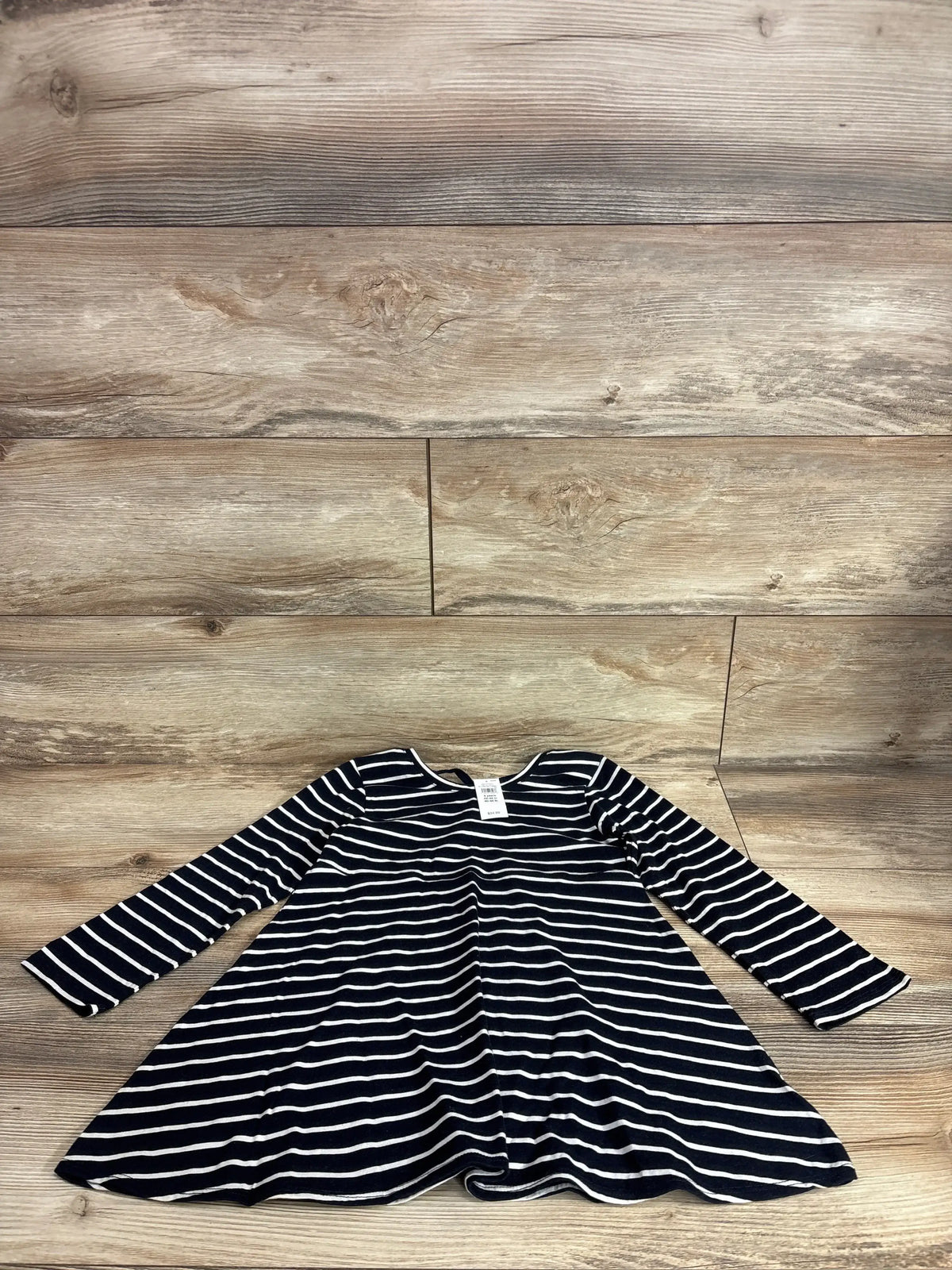 Flat lay of girls’ navy and white striped long-sleeve dress showing flared skirt and crew neckline on wood background