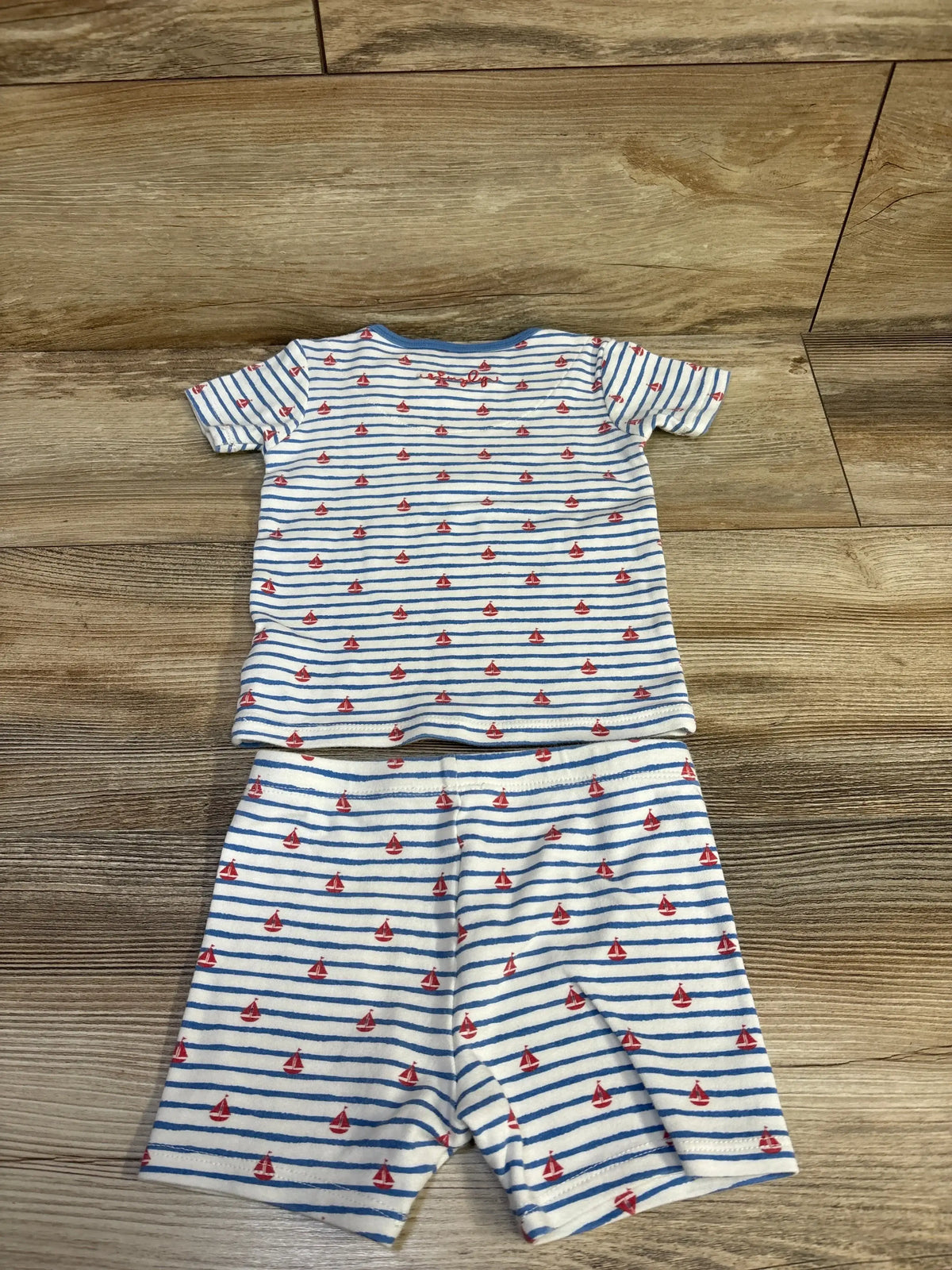 Top-down view of 2-piece toddler pajama set, white with blue stripes and red sailboats, top and shorts on wood floor