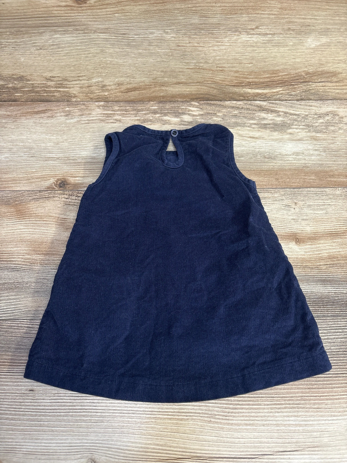 Navy blue sleeveless corduroy toddler dress with button back on wood background