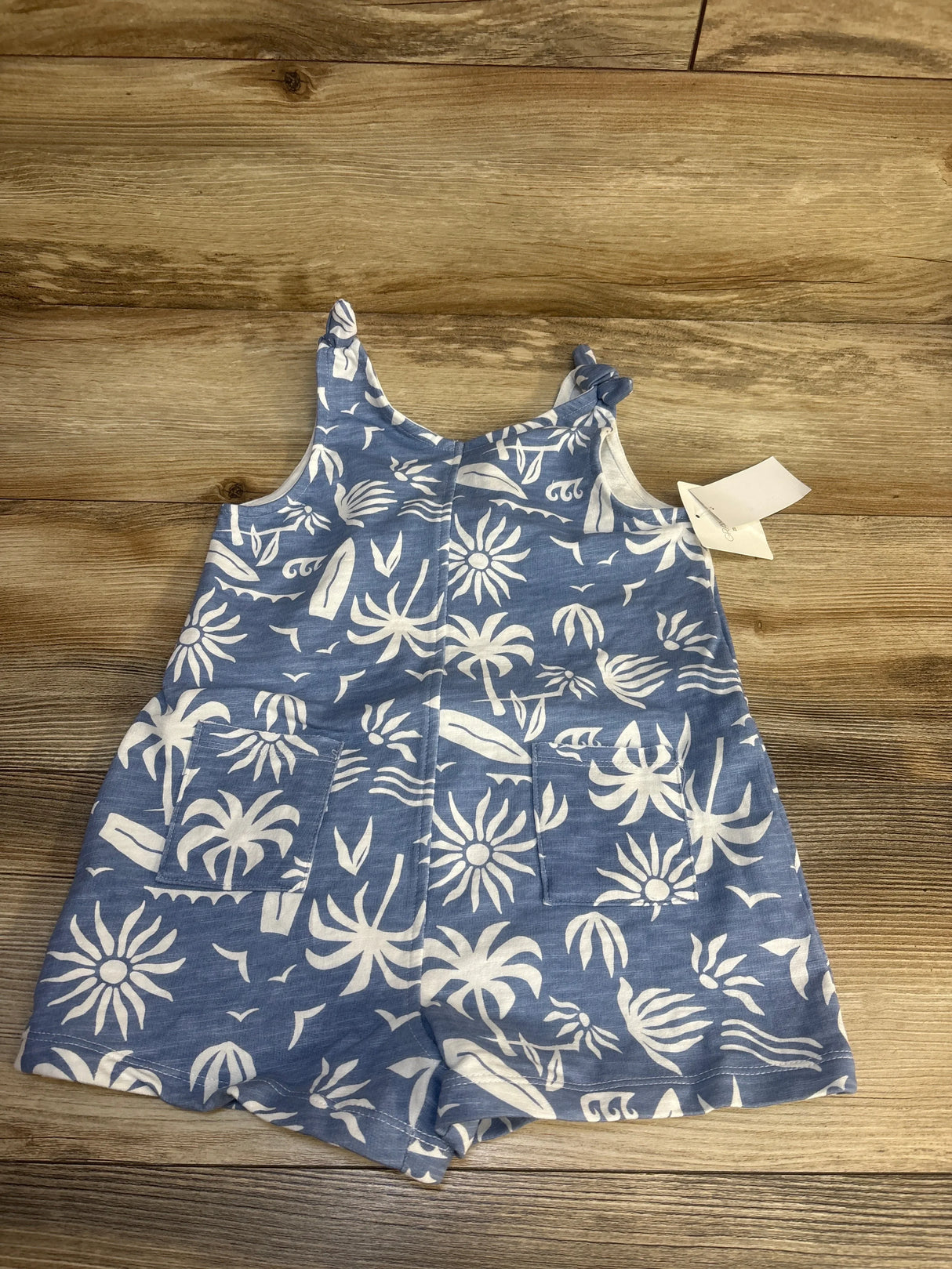 Blue and white baby romper with tropical print and pockets on wooden floor