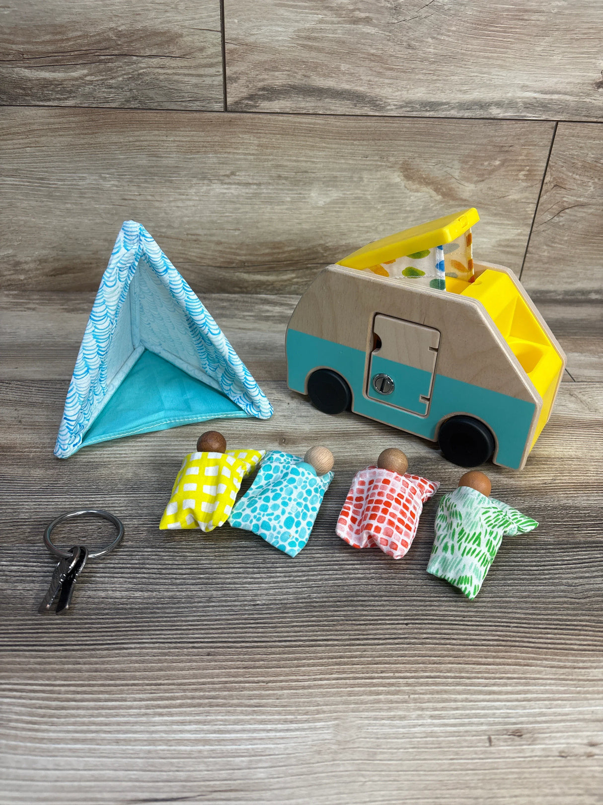 Wooden toy camper set with colorful peg dolls, fabric tent, and key on wood background