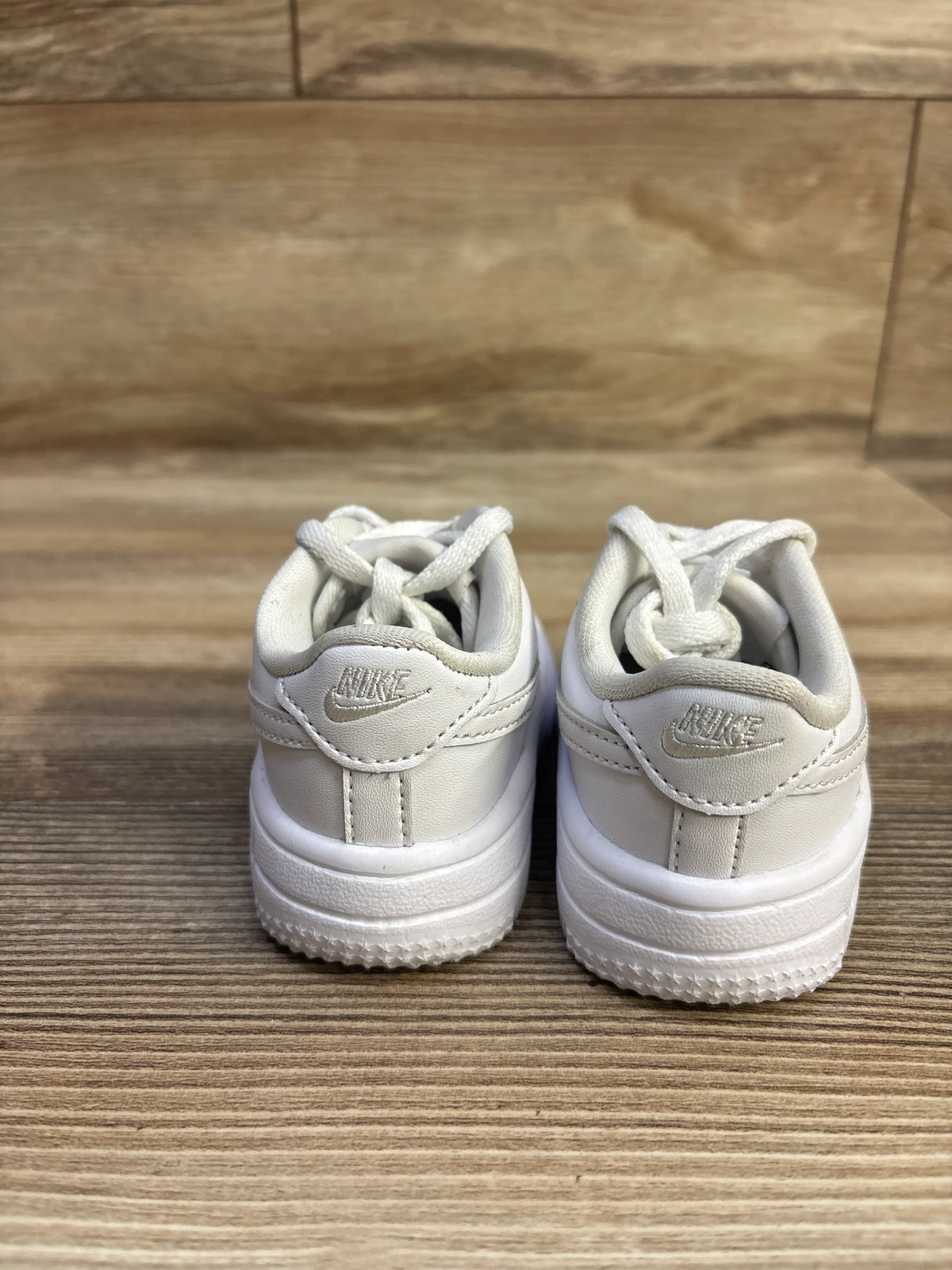 Rear view of Nike Air Force 1 Low toddler sneakers showcasing stitched Swoosh on heels and white leather upper on wood floor