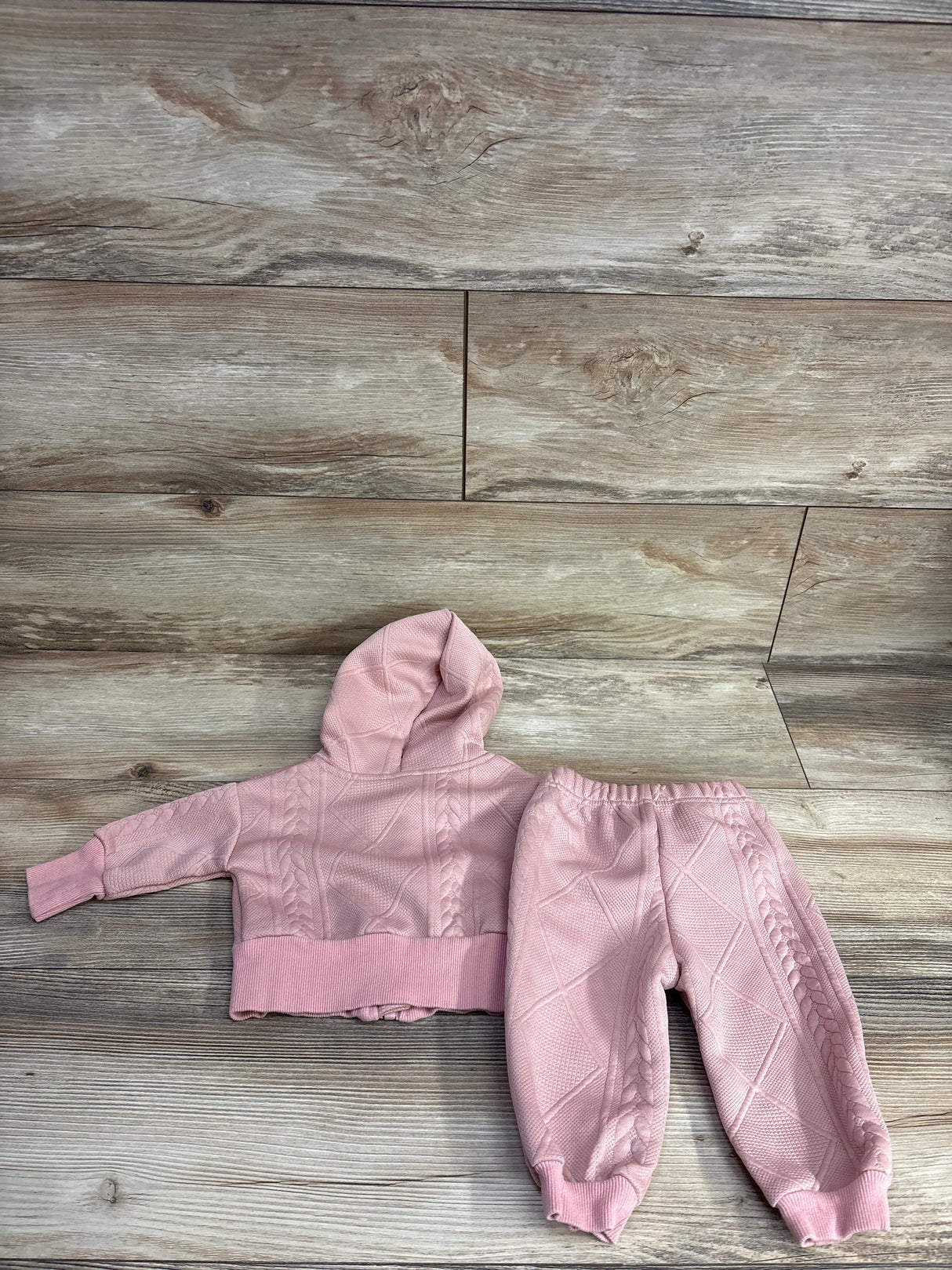 Pink cable knit toddler hoodie and matching pants set on wood floor background