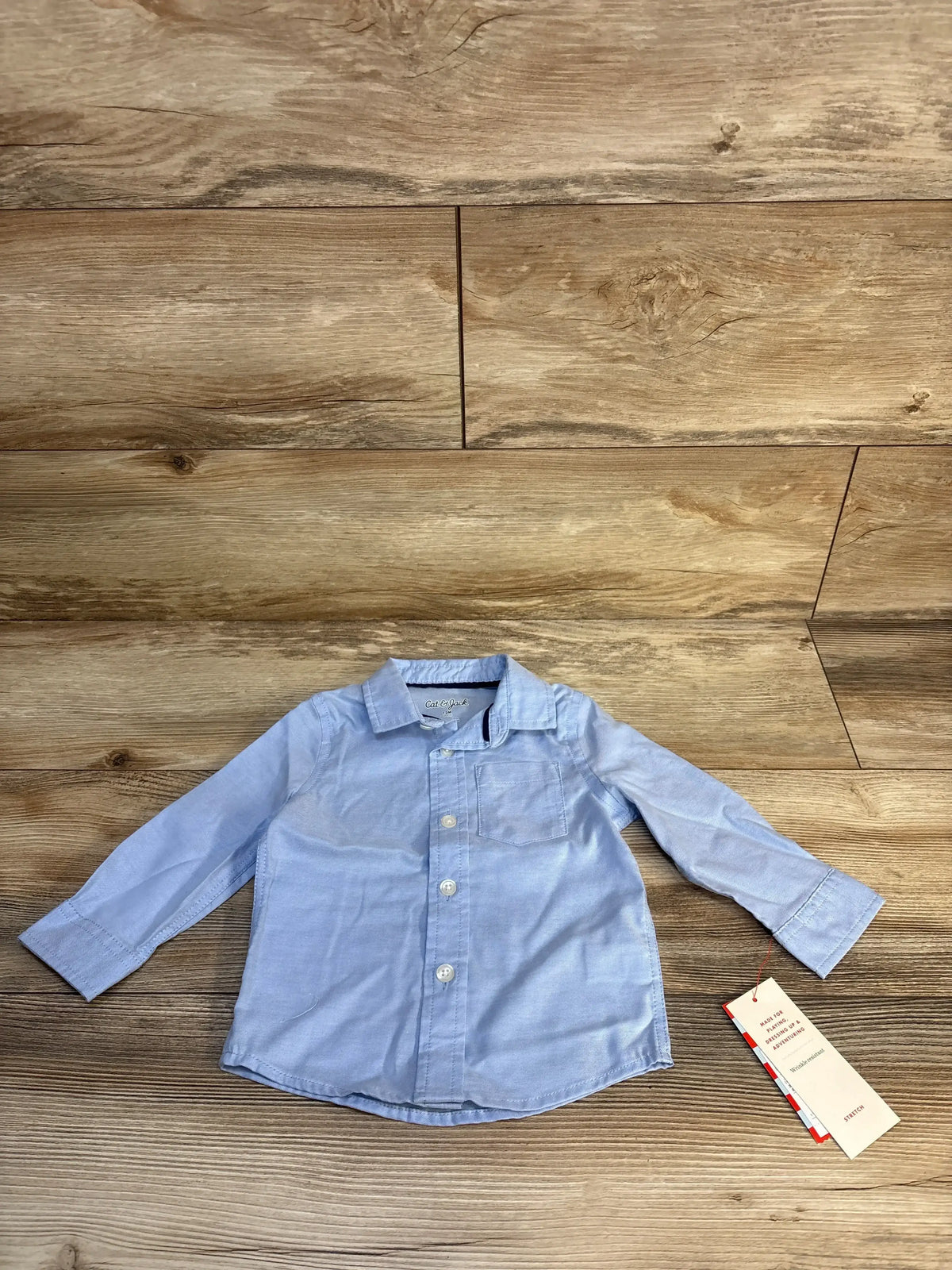 Light blue long sleeve toddler button-up shirt with pocket, displayed on wood background