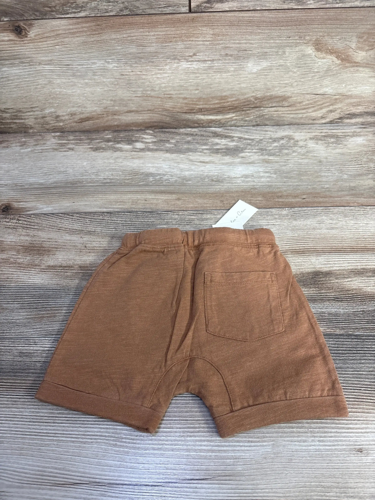 Back view of Rylee and Cru front pouch shorts in caramel showing rear patch pocket and elastic waist on wood plank background