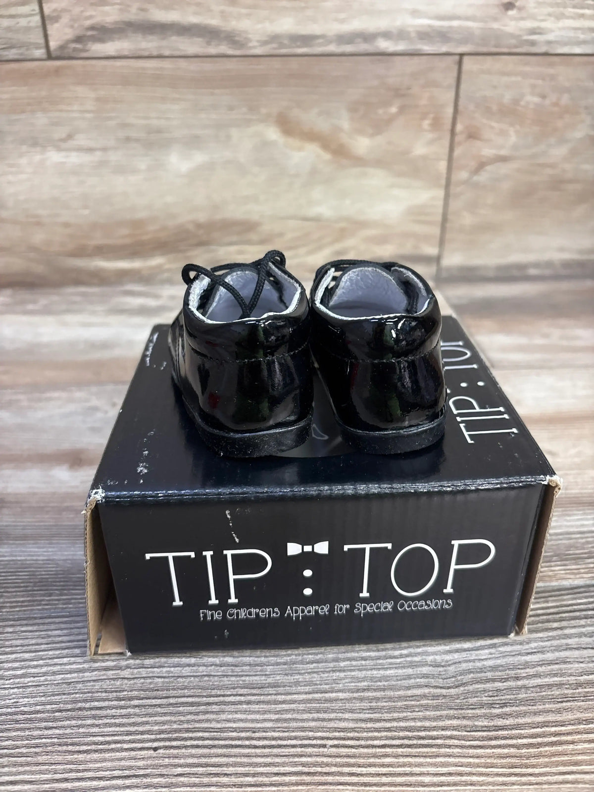 Rear view of Tip Top 308 toddler black patent leather sneakers with glossy finish and laces on Tip Top box