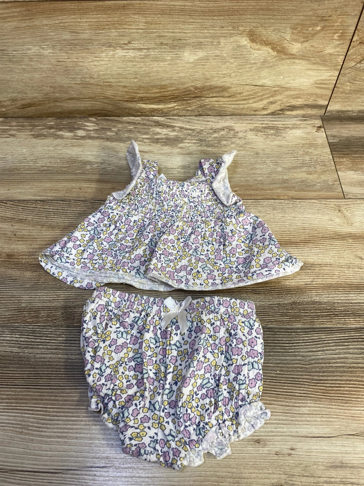 Flat lay of 0-3M two-piece smocked floral top and bloomers showing ruffle straps and elasticized legs on wood background
