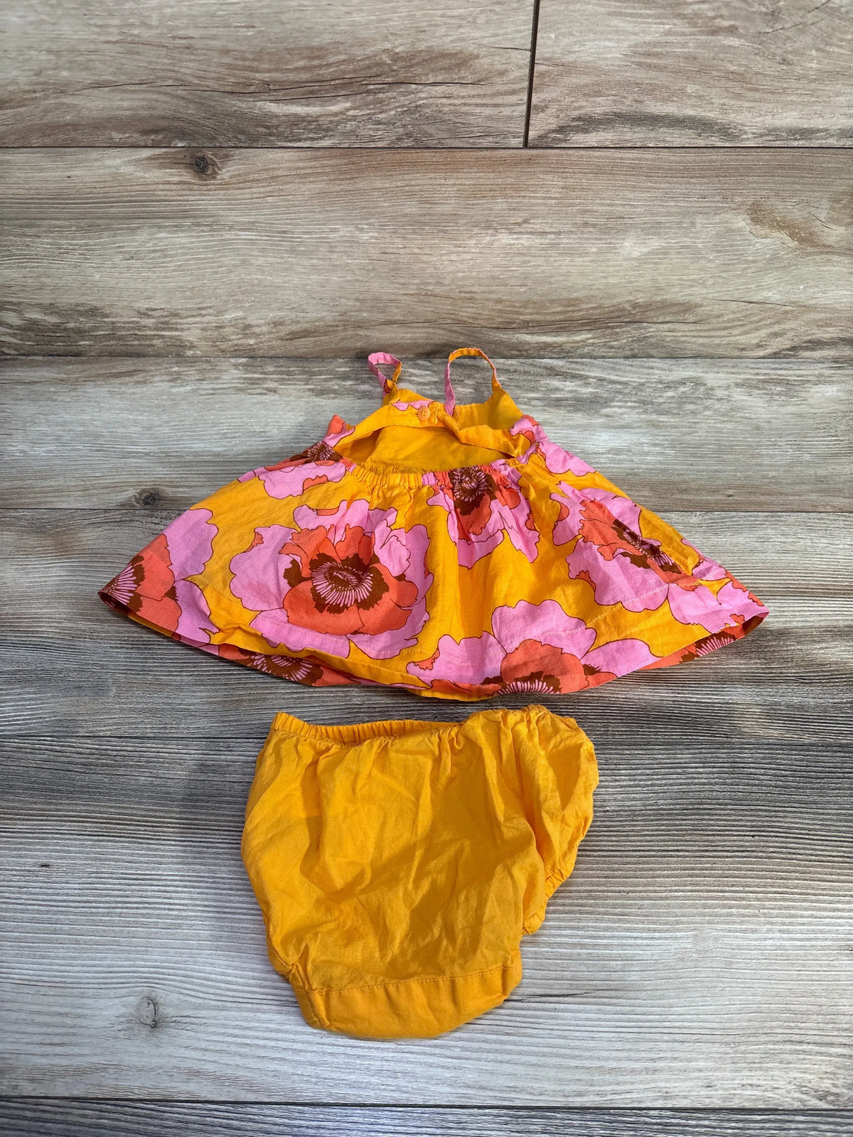 Top view of Baby Gap two-piece floral dress and bloomers set showcasing orange floral print with a wood-look background