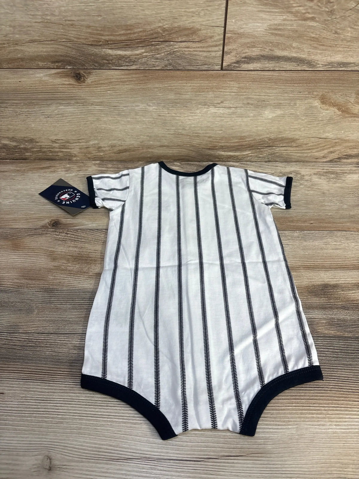 Flat lay of white 24M baby romper showcasing navy pinstripes and navy ribbed trim with wood background