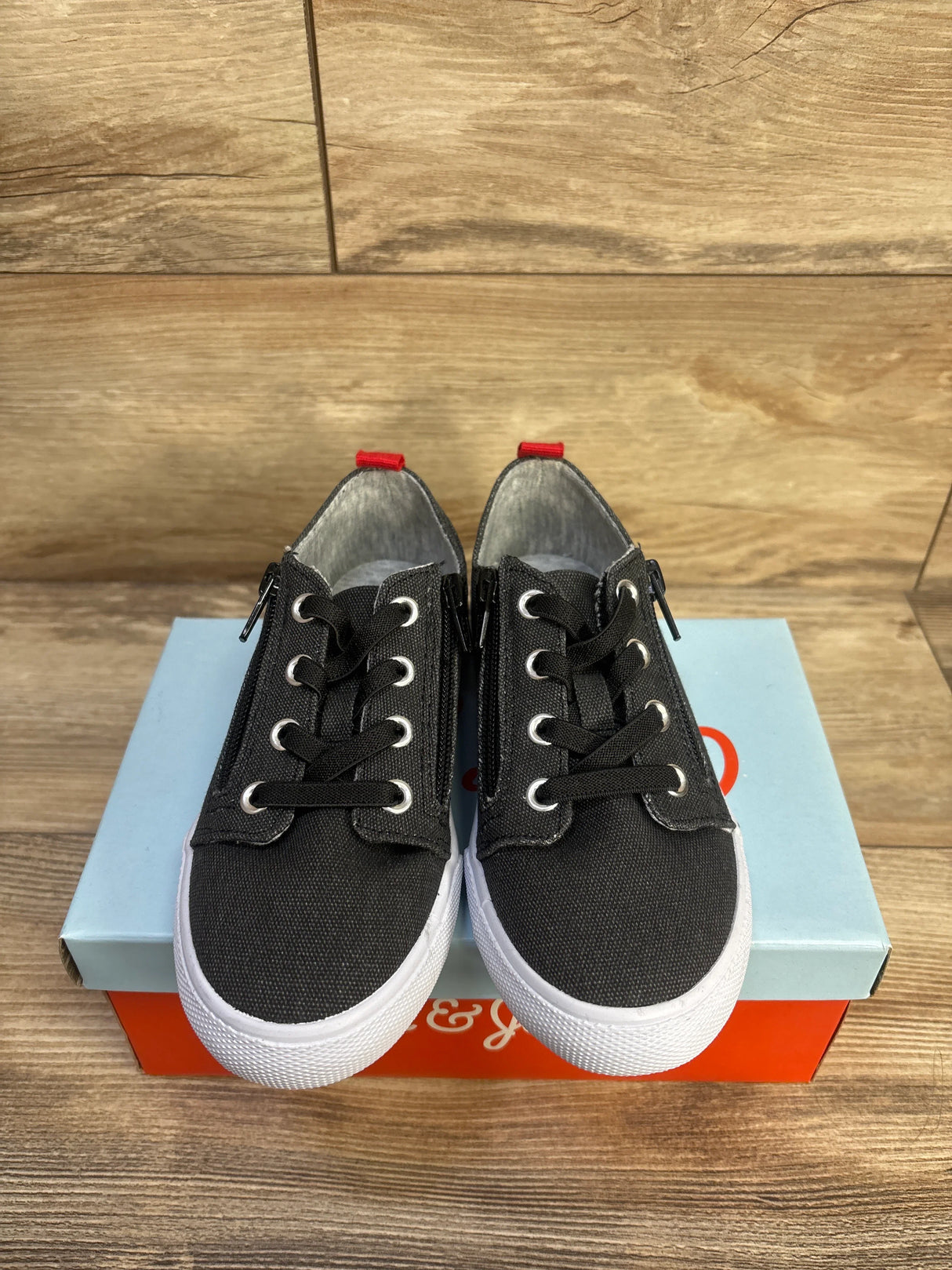 Top-front view of Cat & Jack toddler sneakers with double side zippers, black canvas upper and white rubber sole on a shoe box