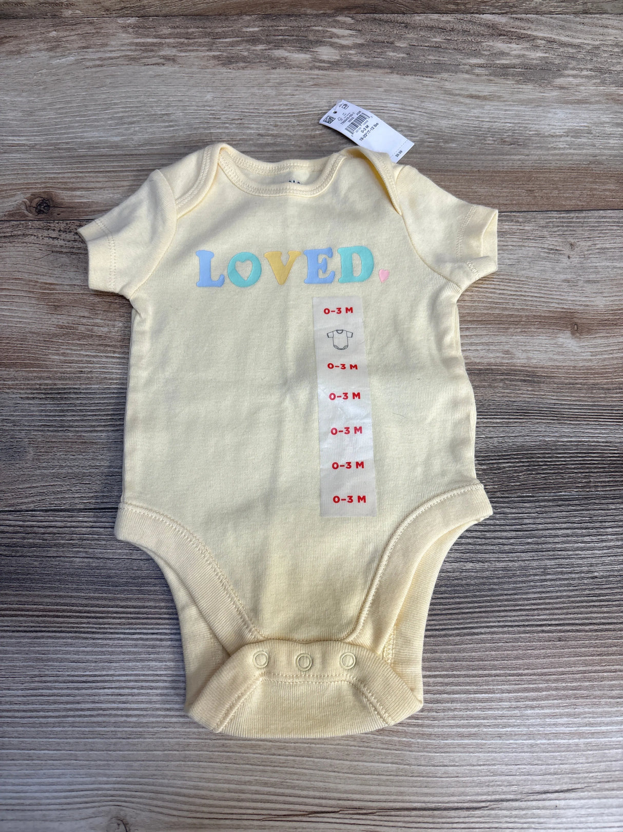 Yellow baby onesie with 'LOVED' text, size 0-3 months, displayed on wood background