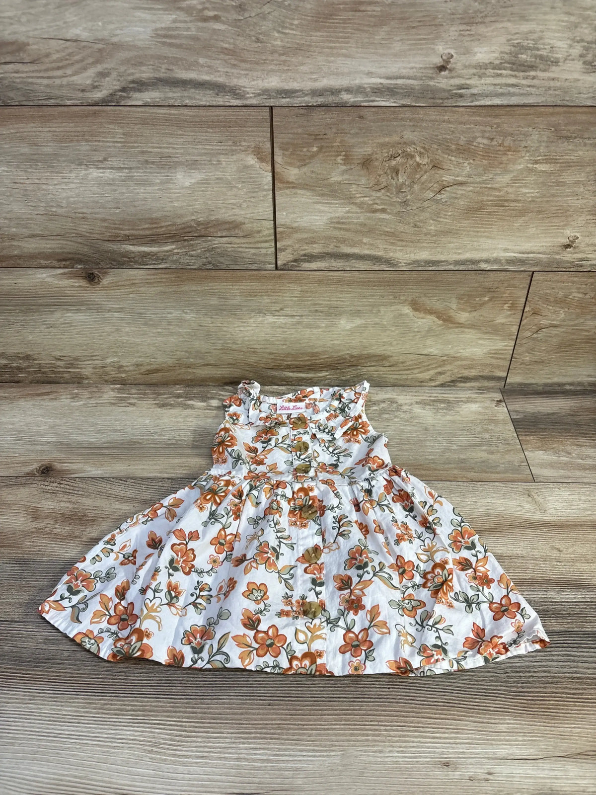 Front view of Little Lass white floral dress showcasing sleeveless 100% cotton design and button front on wood floor