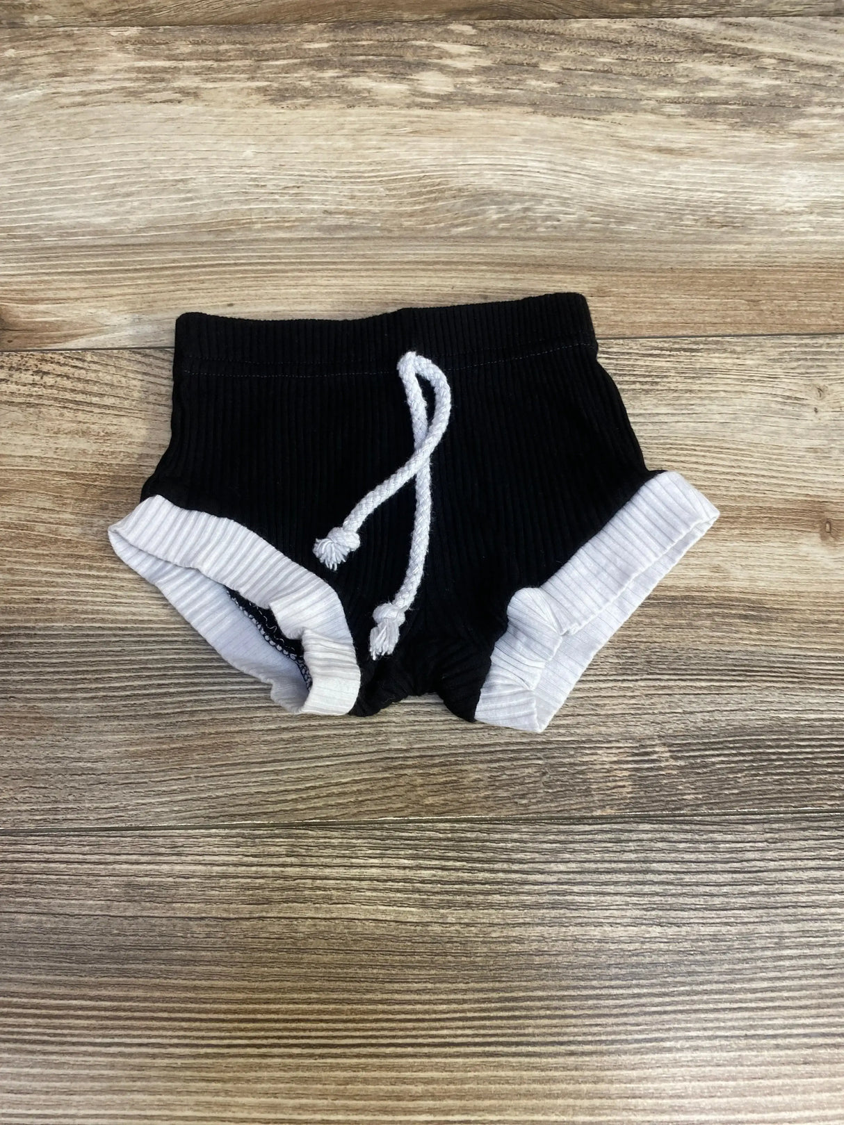 Top-down view of black ribbed baby bloomers size 3M showing white rolled cuffs and knotted drawstring on wood background