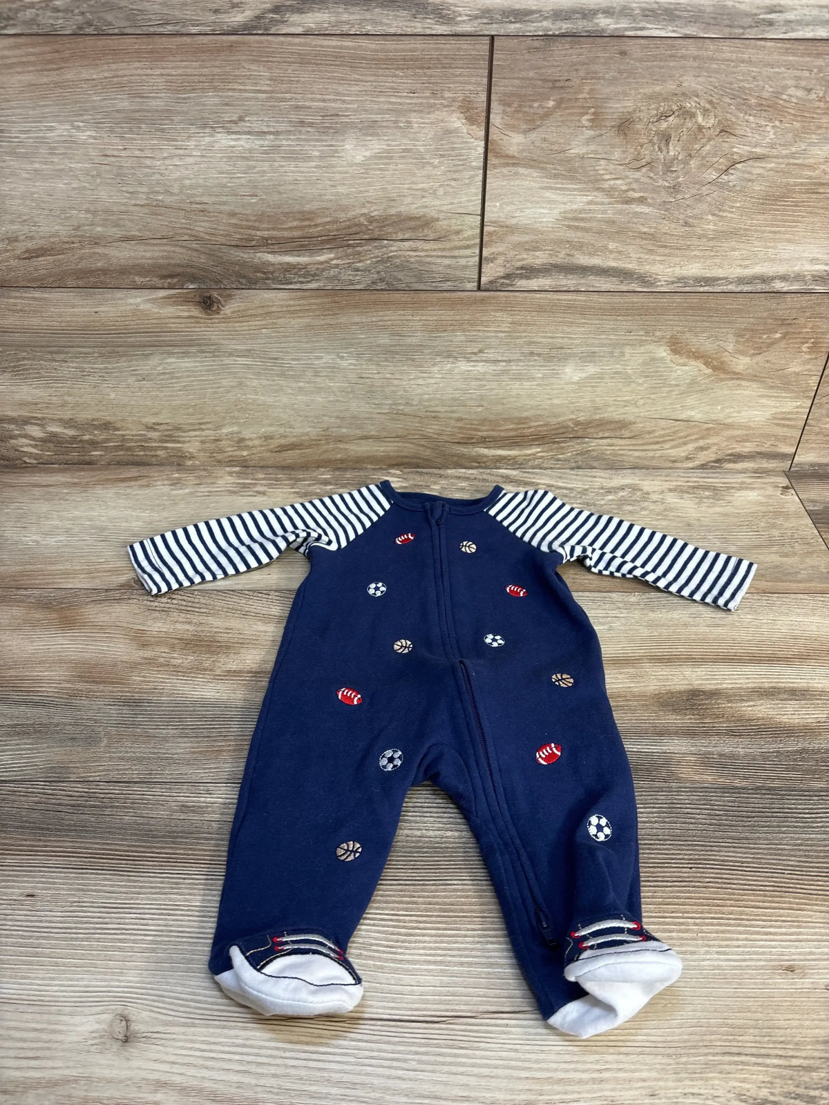 Navy baby onesie with sports ball print, striped sleeves, and footies on wood floor