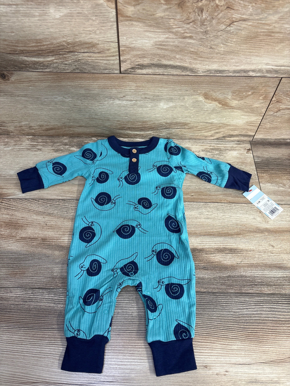 Blue baby onesie with navy snail prints and wooden buttons on wooden floor