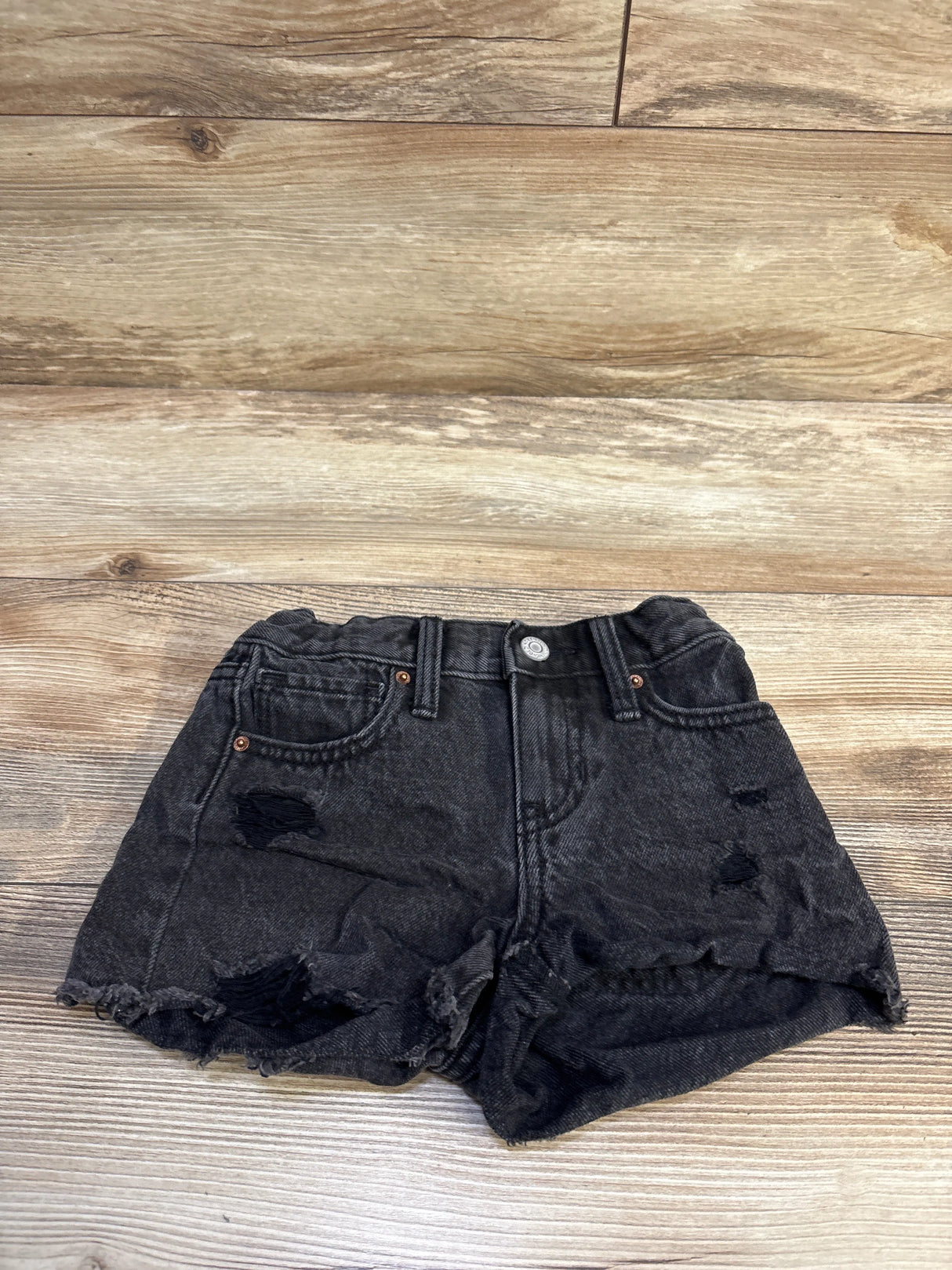 Flat lay of Old Navy high-rise black distressed denim shorts 5T showing frayed hem and rips on light wood background