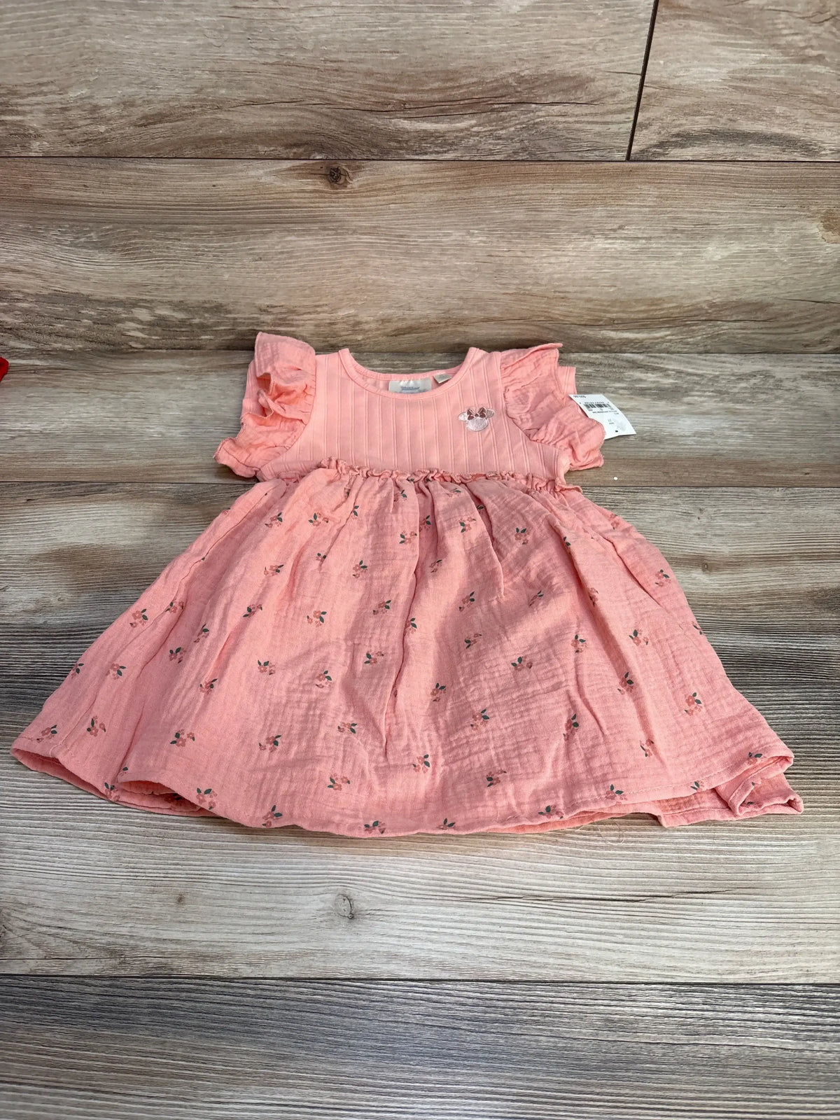 Flat lay of pink Disney Minnie Mouse muslin toddler dress (size 2T) showcasing flutter sleeves, gathered waist and small floral print on wood floor