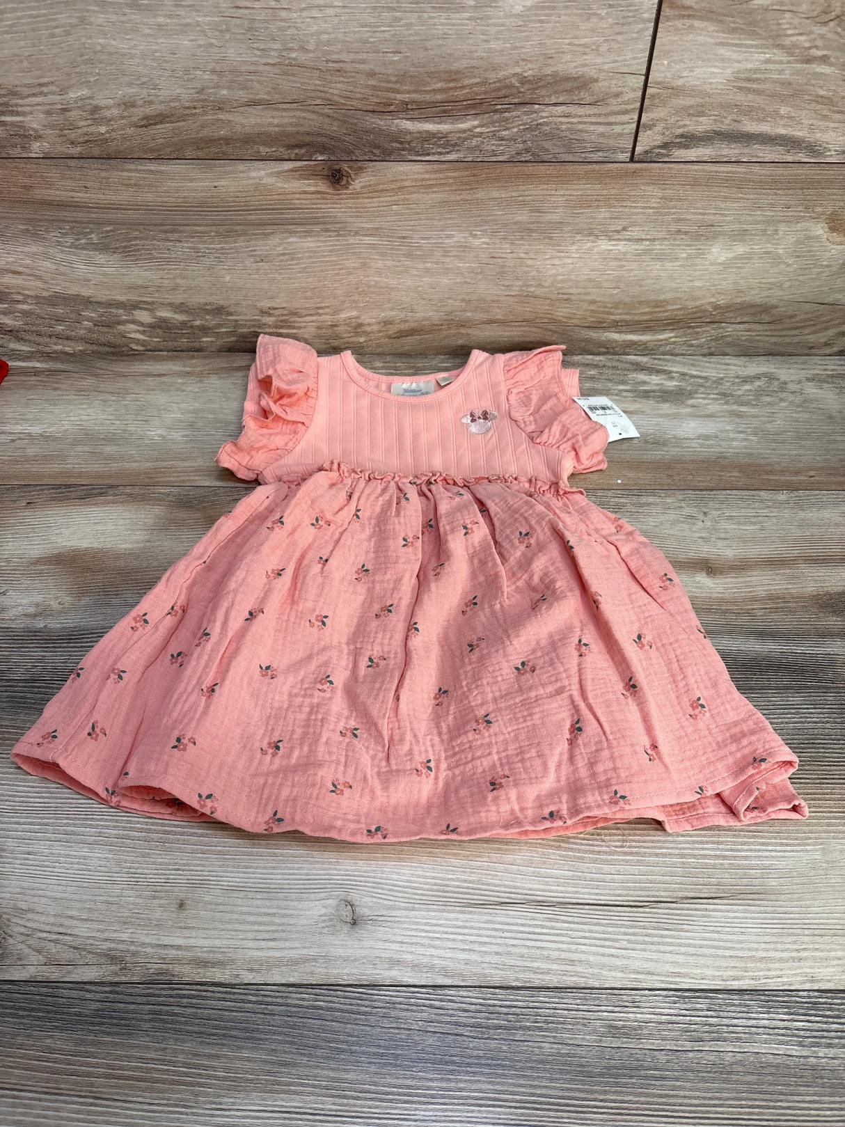 Flat lay of pink Disney Minnie Mouse muslin toddler dress (size 2T) showcasing flutter sleeves, gathered waist and small floral print on wood floor