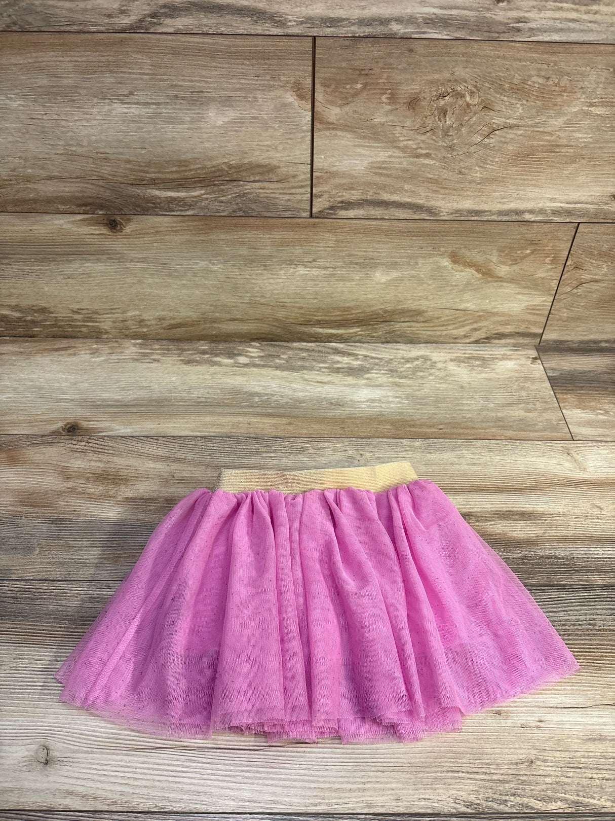 Flat lay of pink tulle toddler skirt showcasing gold elastic waistband and layered glitter tulle on light wood background
