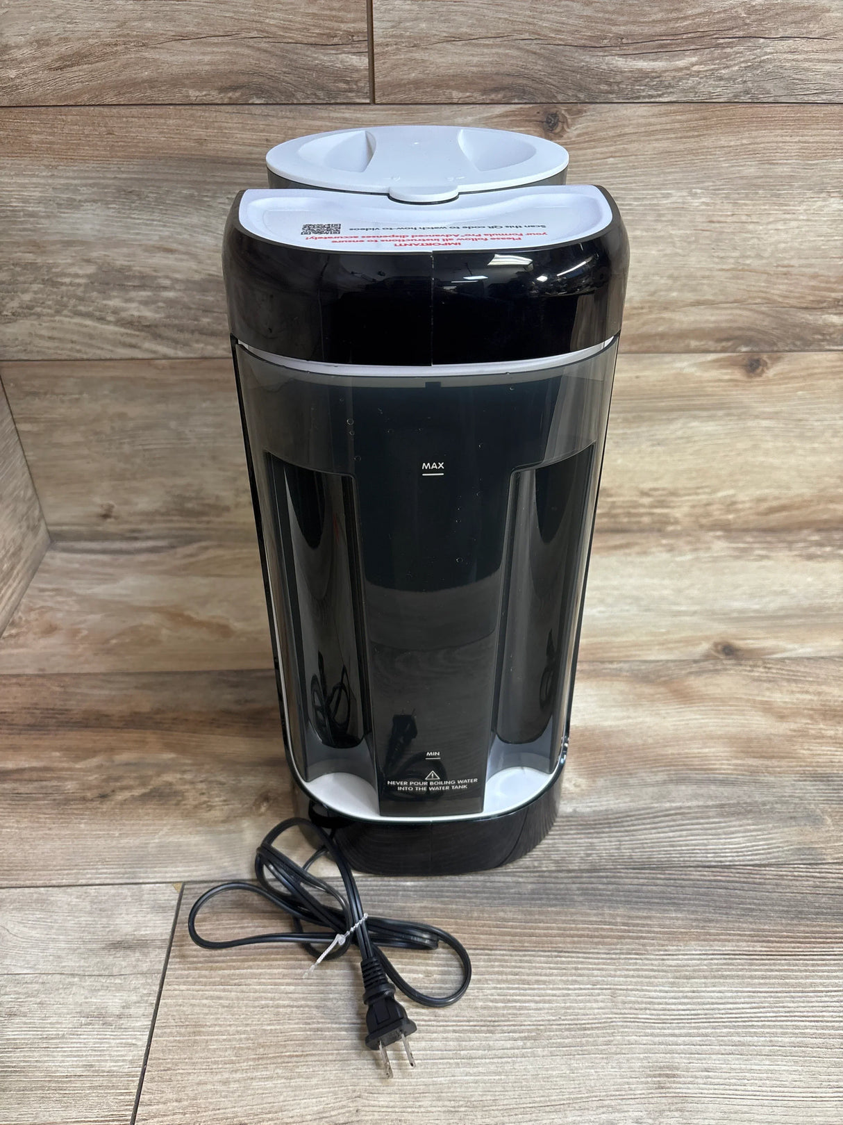 Black and white electric water dispenser with visible water level indicator and attached power cord on wooden surface