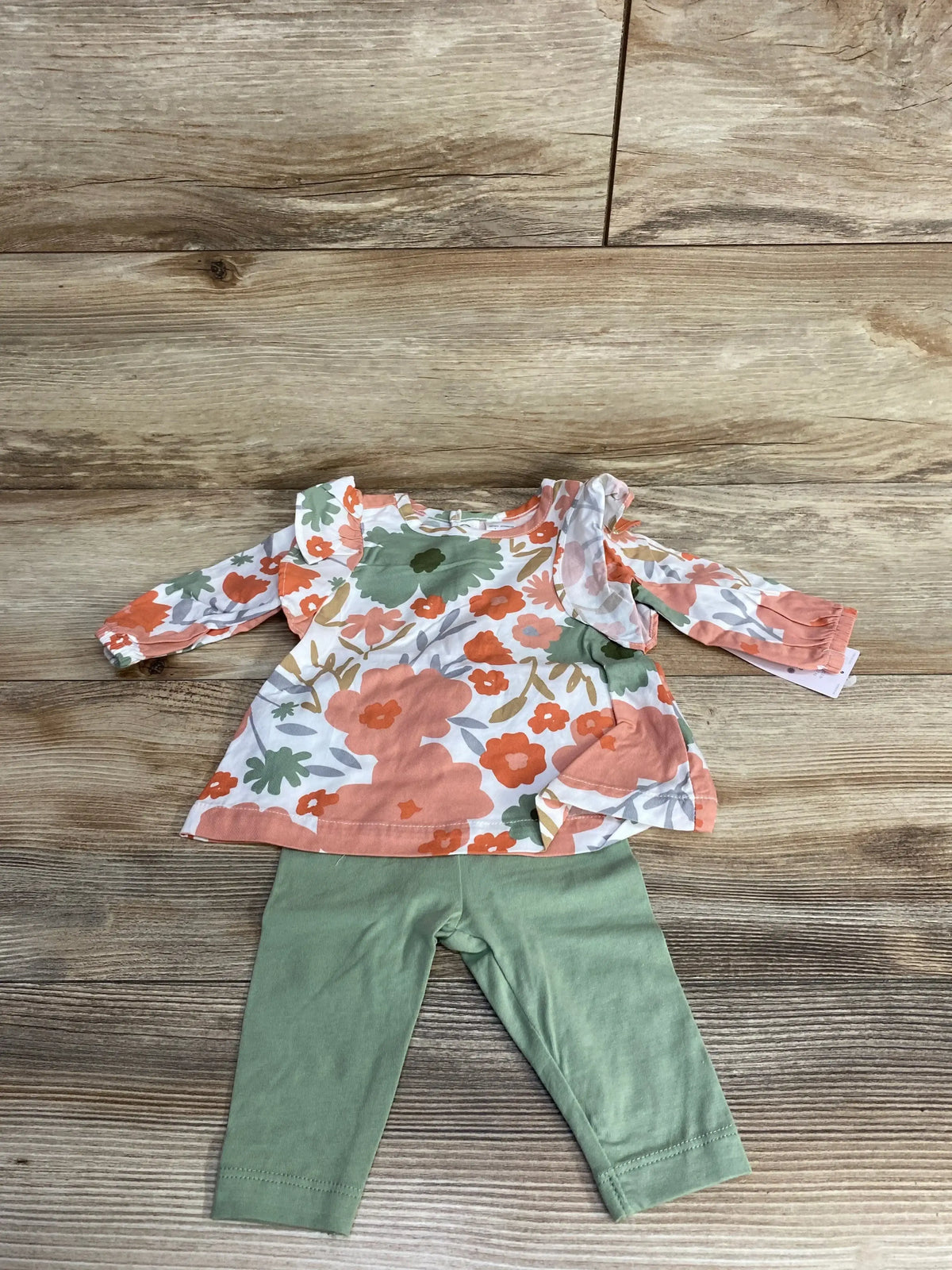 Children's floral long-sleeve top with ruffles and green leggings on wooden floor