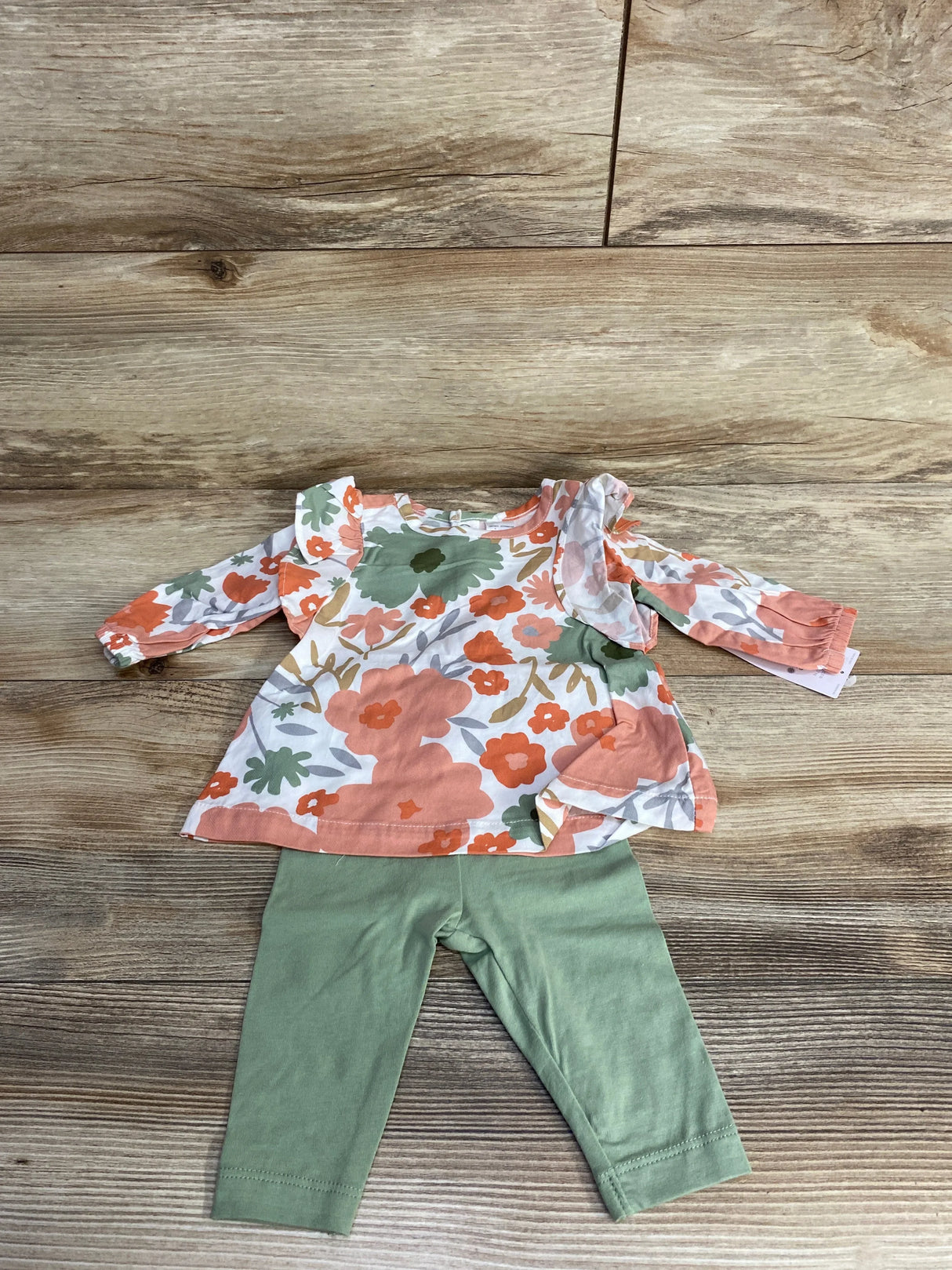 Children's floral long-sleeve top with ruffles and green leggings on wooden floor