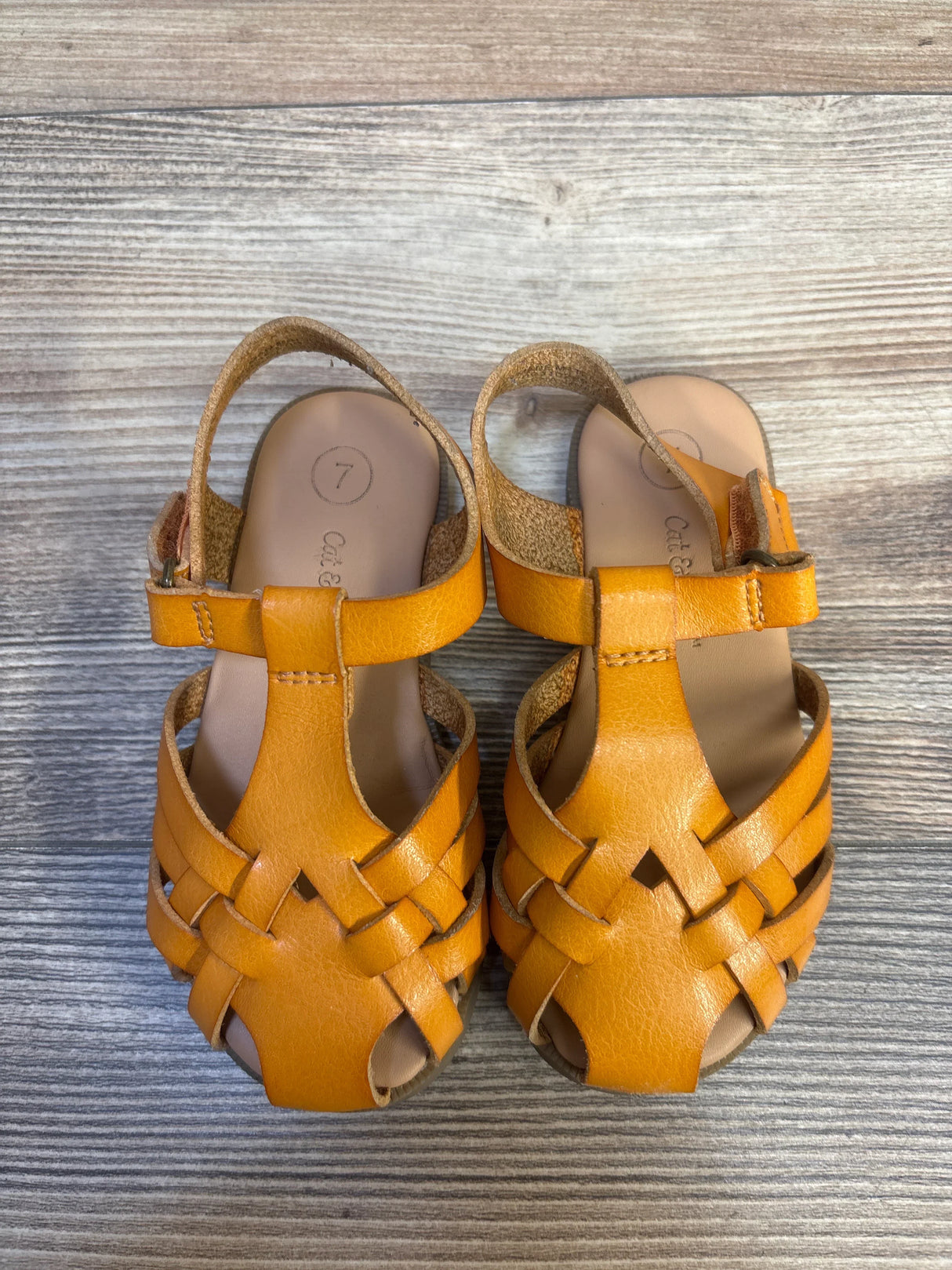 Pair of tan toddler woven leather sandals with ankle straps on wood background